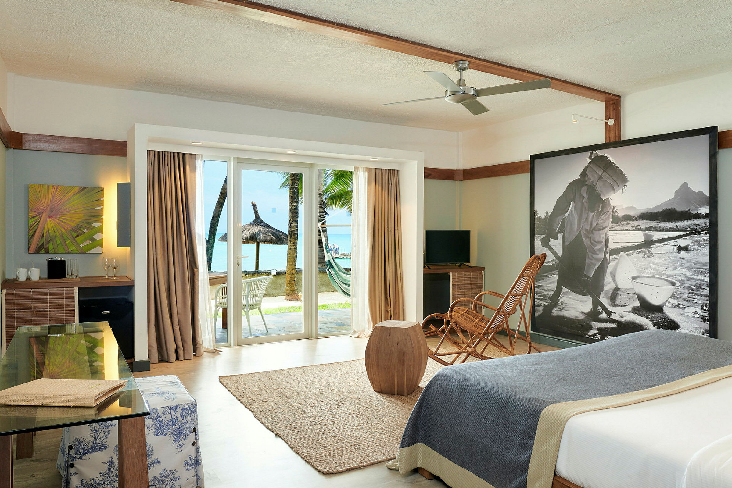 Ett hotellrum med modern inredning, glasdörrar som öppnar upp till strand och palmträd. (AI-genererad text)