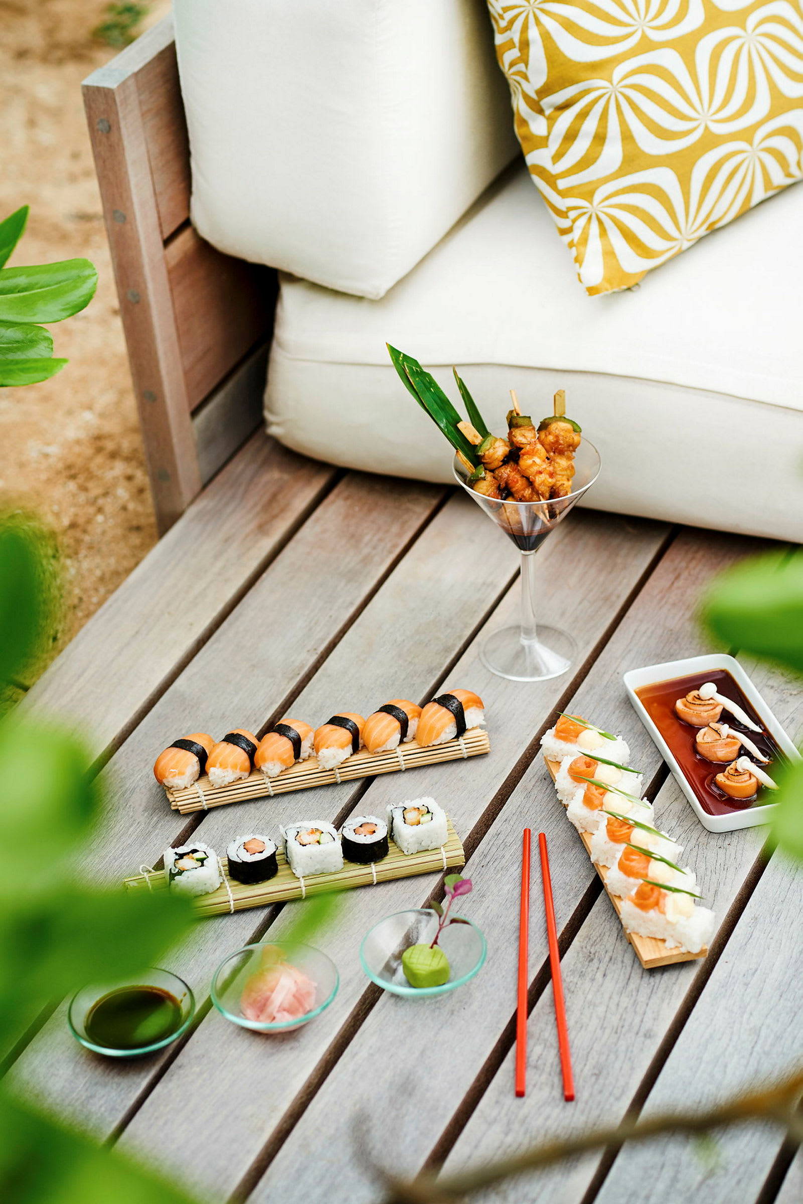 Ett bord med sushi, grillspett och tillbehör bredvid en vit soffa. (AI-genererad text)