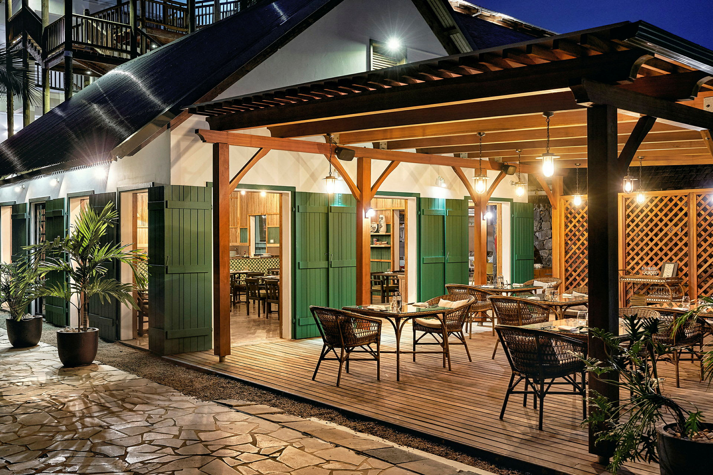 En utomhusrestaurang med bord och stolar under en träpaviljong med belysning. (AI-genererad text)