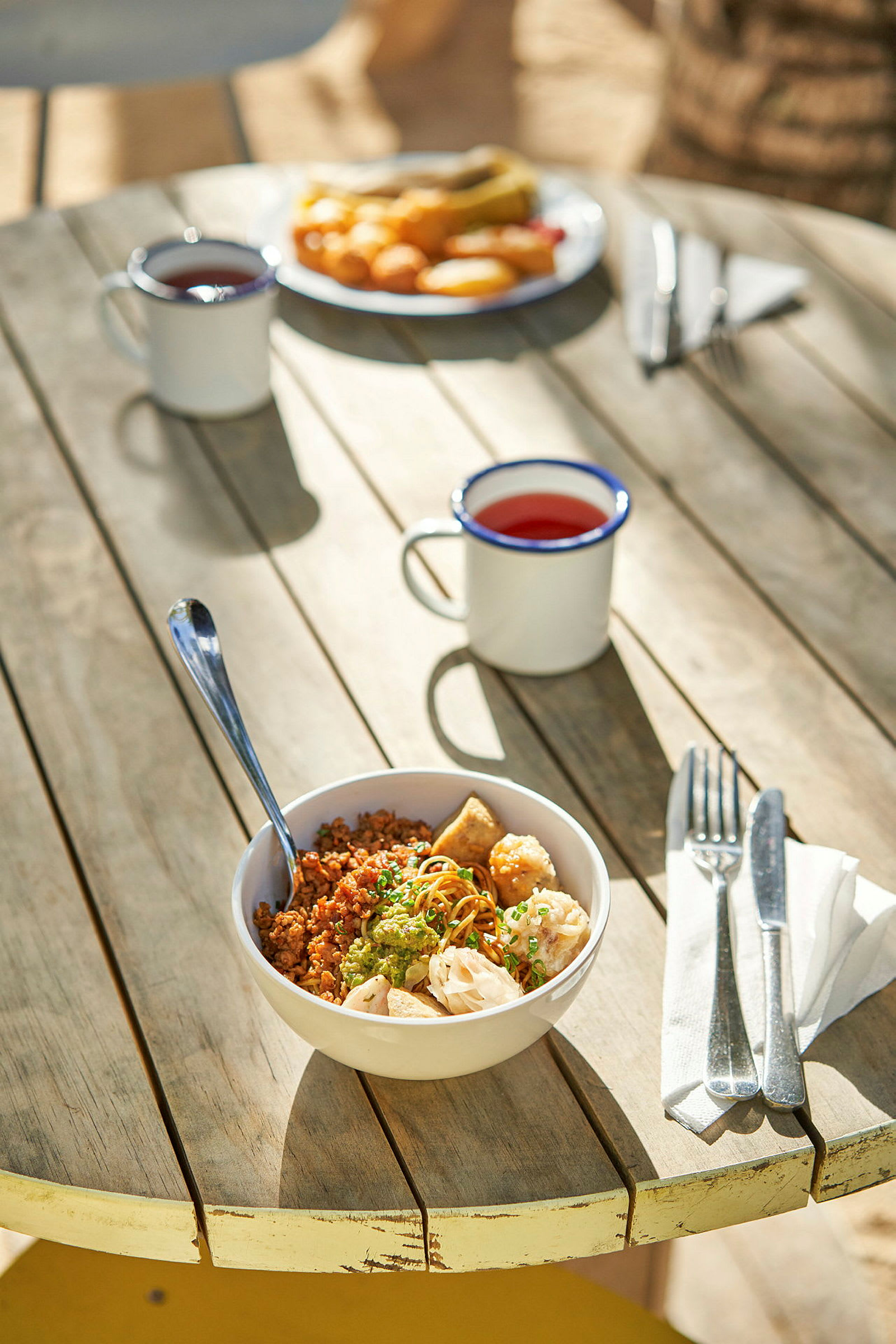 En skål med mat samt en mugg och bestick på ett träbord. (AI-genererad text)