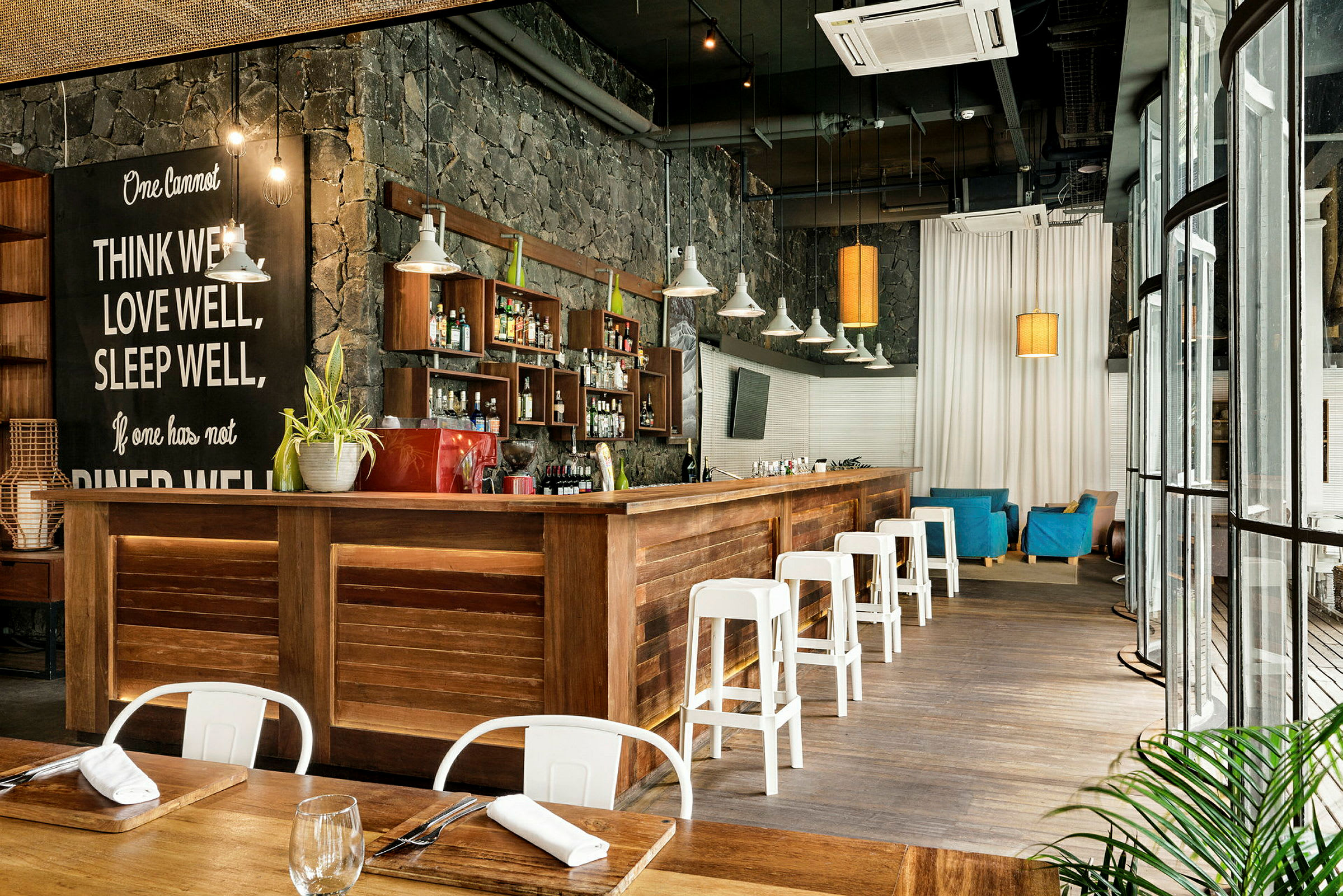En interiör av en modern bar med träinredning, vita stolar och en stenmur. (AI-genererad text)