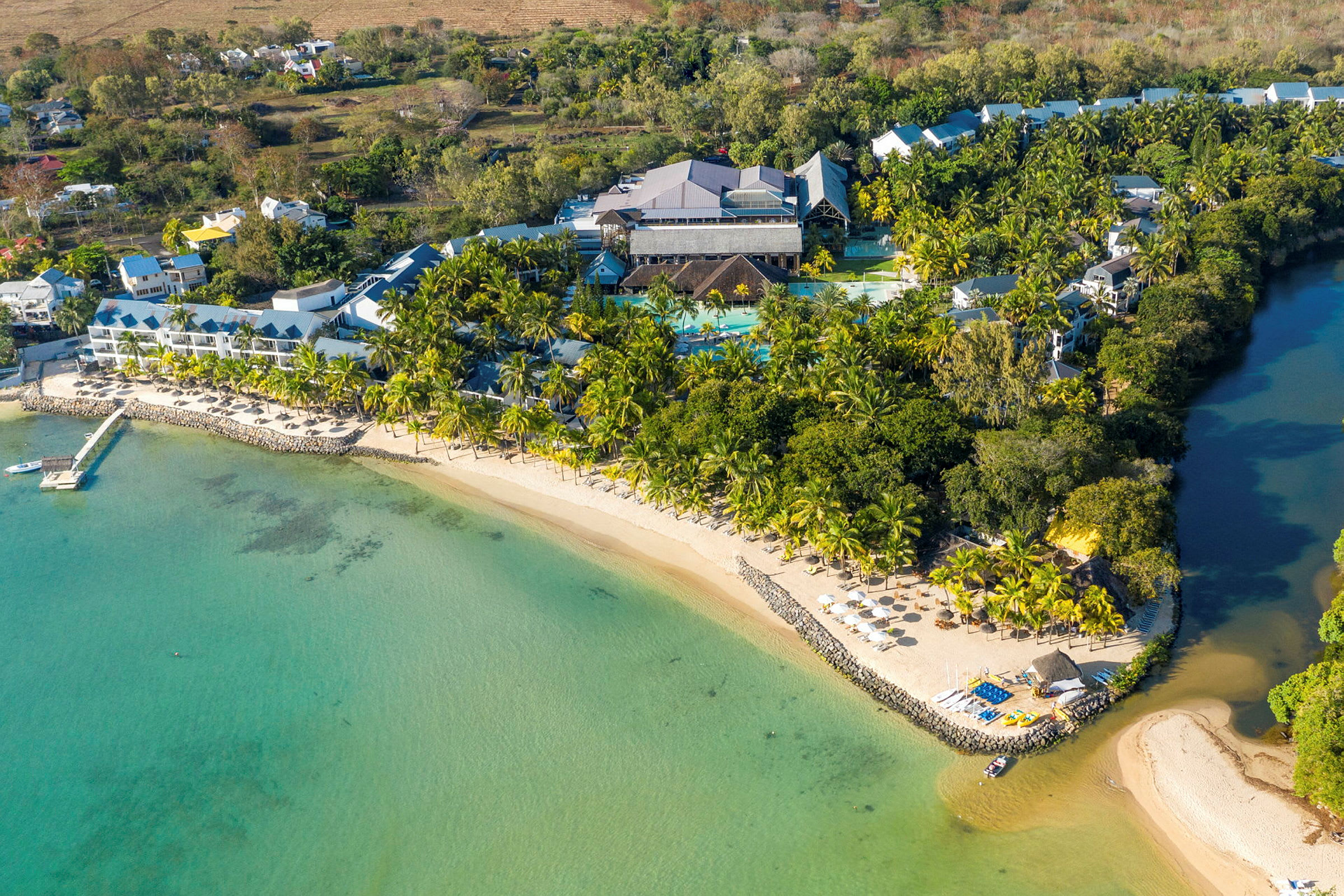 Flygfoto av en tropisk resort vid en sandstrand med turkost vatten och grönområden. (AI-genererad text)