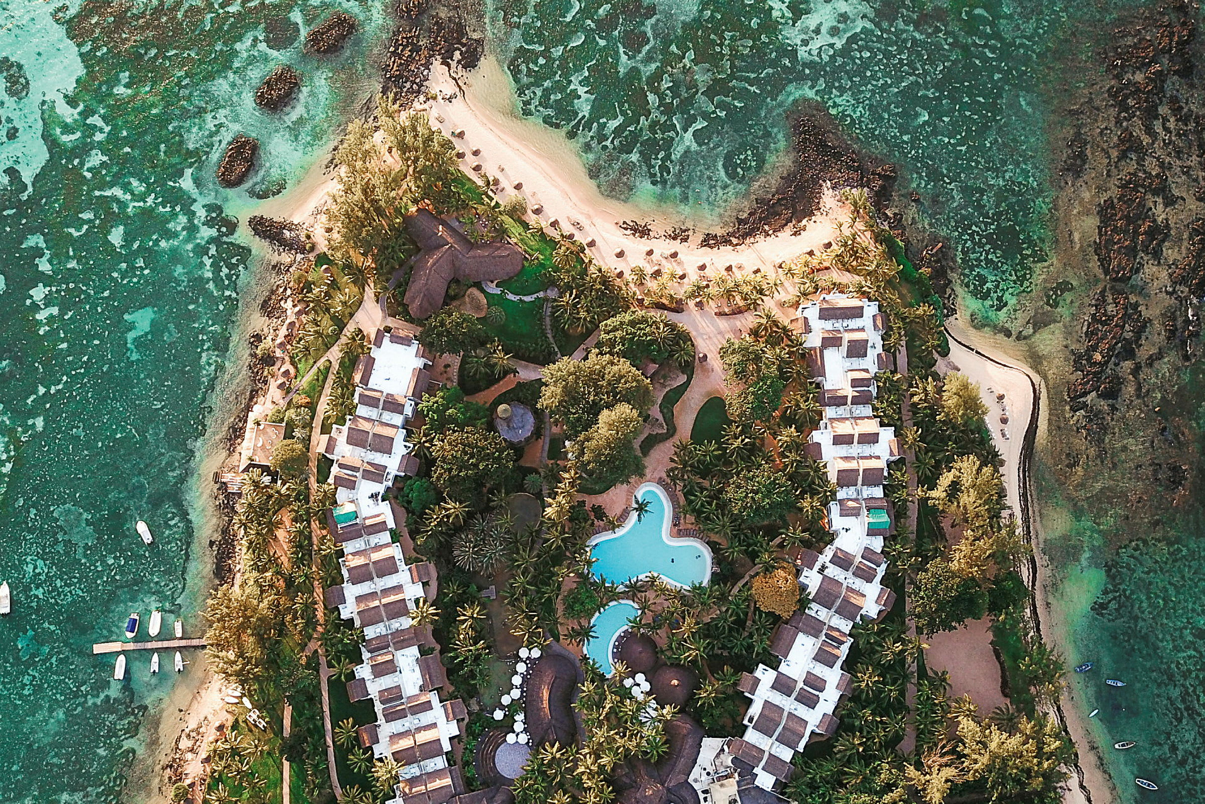 Flygbild över ett semesterresort med pool och omgivande grönska vid kusten. (AI-genererad text)