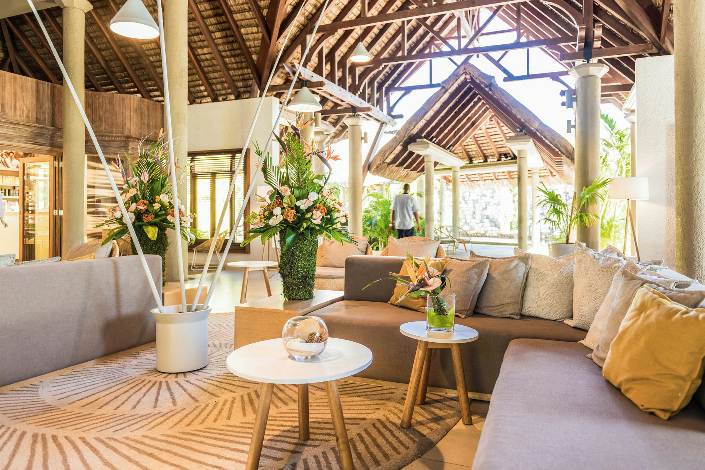 Interiören i en rymlig och ljus lounge med soffor, blommor och takbjälkar. (AI-genererad text)