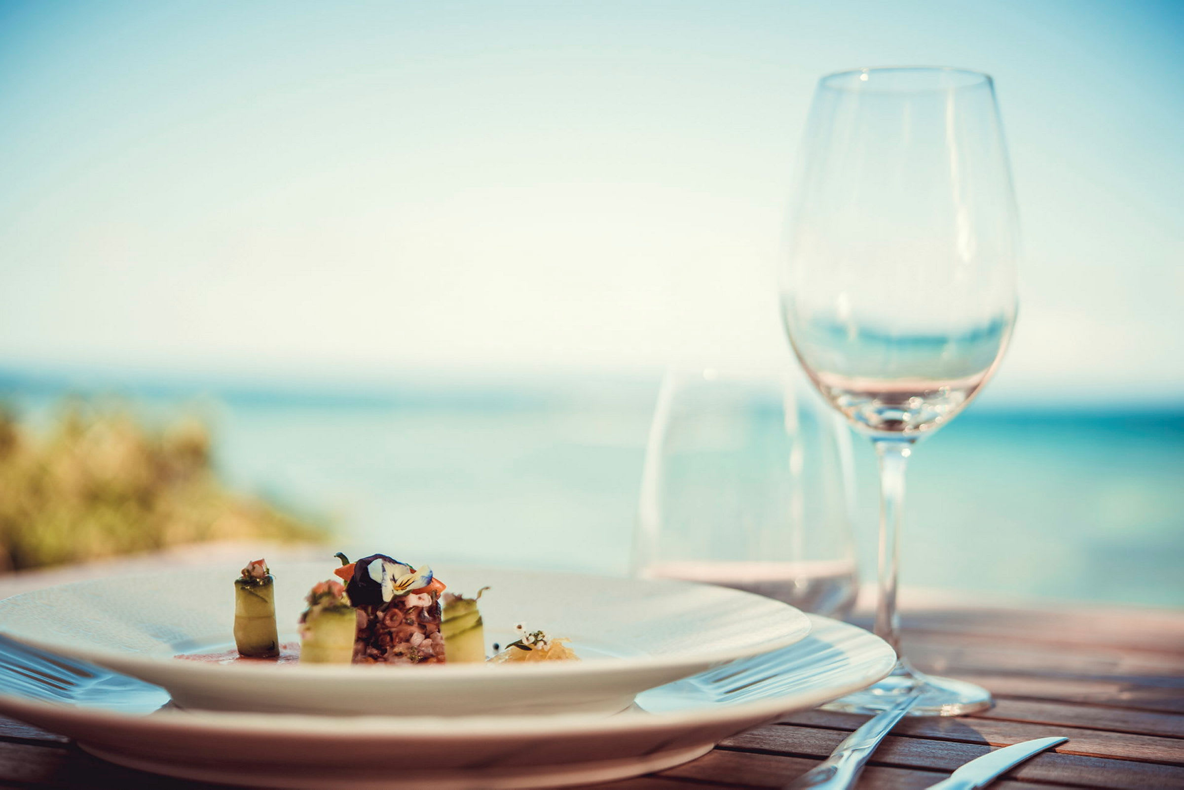 En tallrik med en elegant maträtt och ett glas på ett bord med havsutsikt. (AI-genererad text)