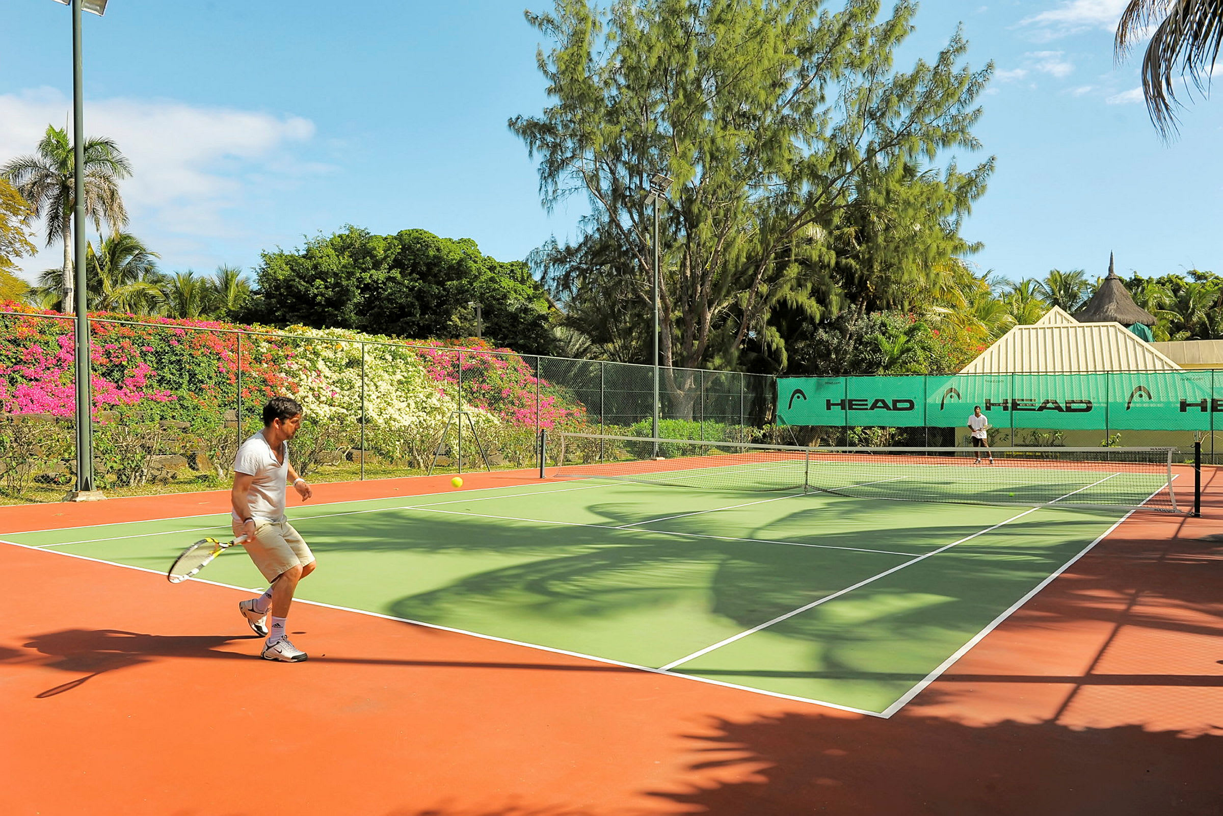 En tennisbana omgiven av grönska och färgglada blommor. (AI-genererad text)