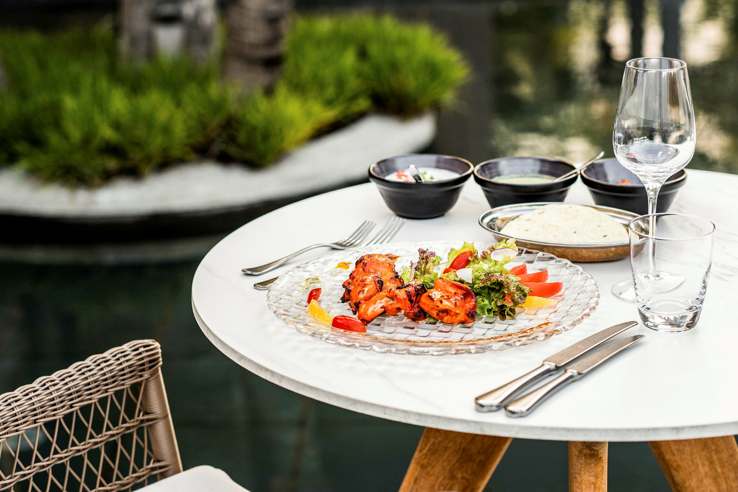 Ett bord utomhus med tallrikar fyllda med mat, glas och bestick. (AI-genererad text)