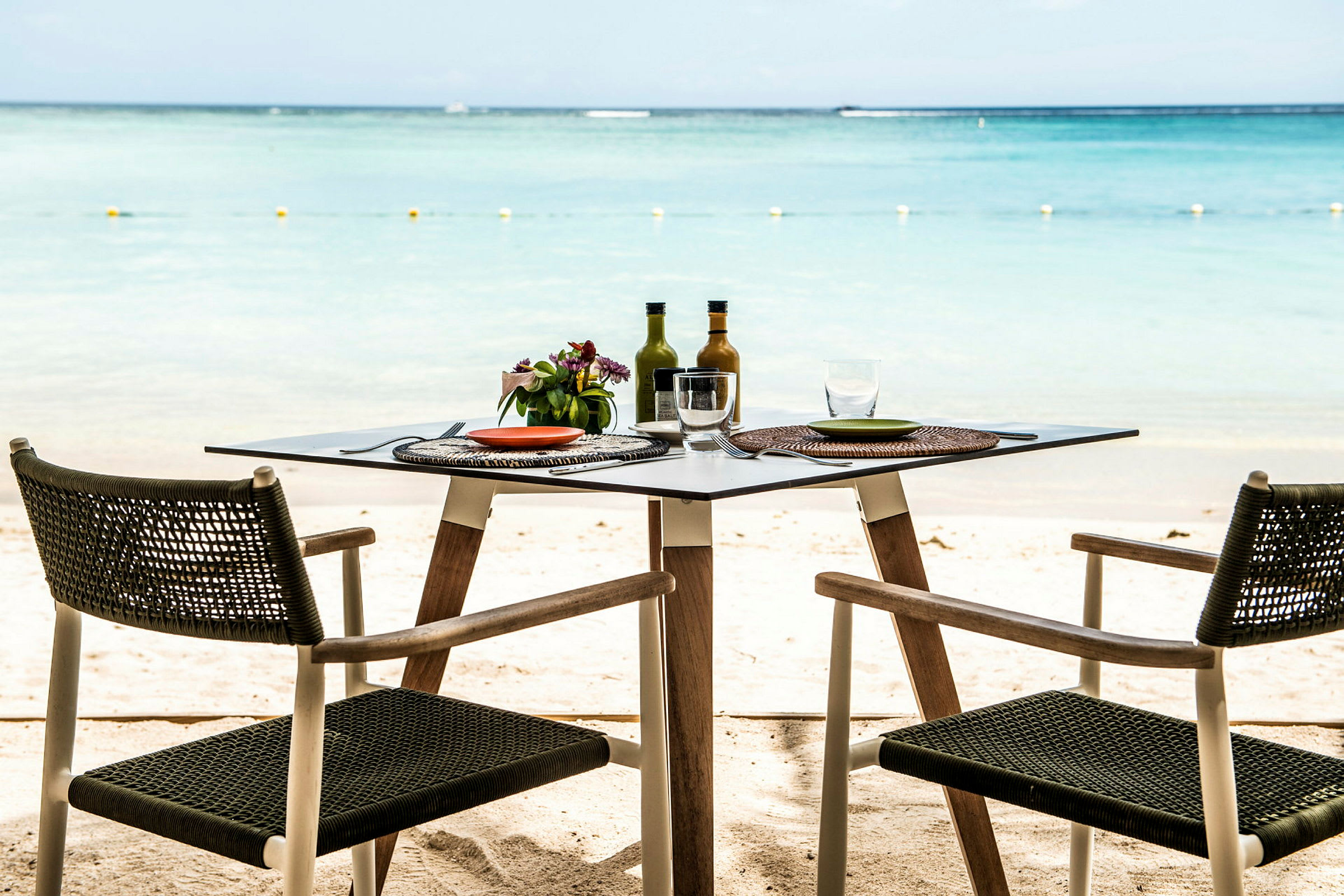 Två stolar och ett dukat bord står på en sandstrand med utsikt över havet. (AI-genererad text)