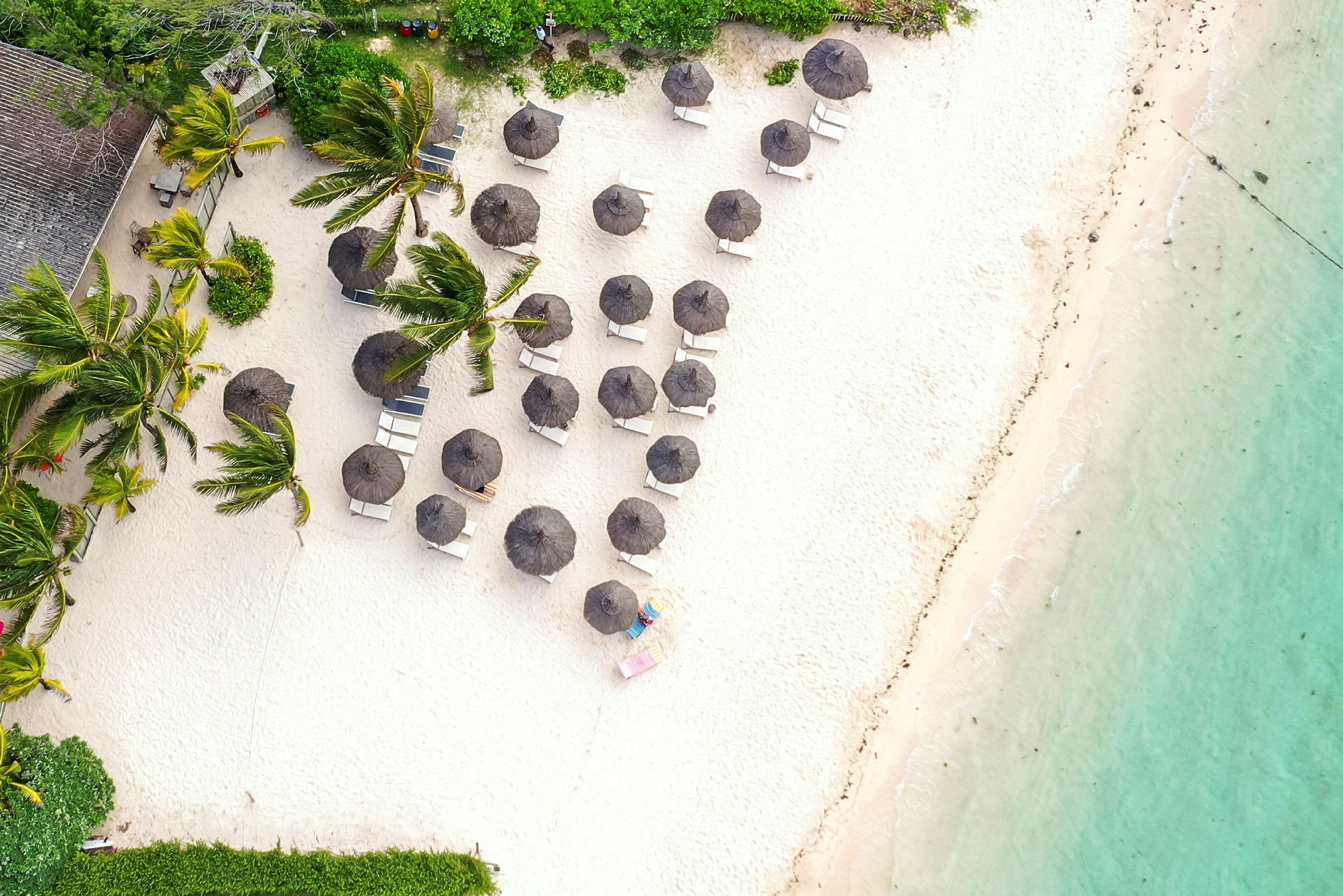 Flygbild av en sandstrand med solstolar och parasoller nära vatten och vegetation. (AI-genererad text)