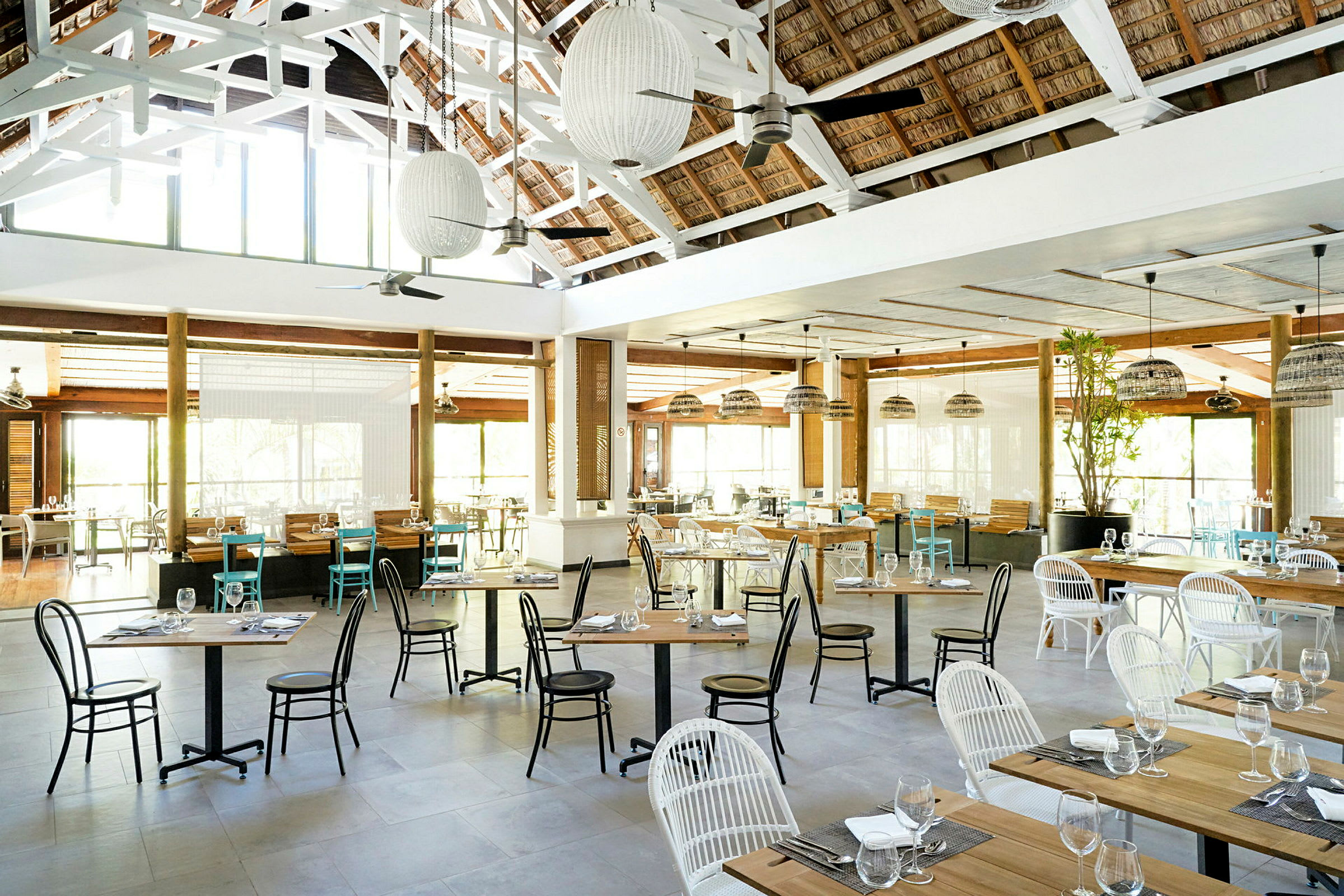 En rymlig restaurang med bord och stolar, dekorerad med lampor och med stora fönster som släpper in ljus. (AI-genererad text)