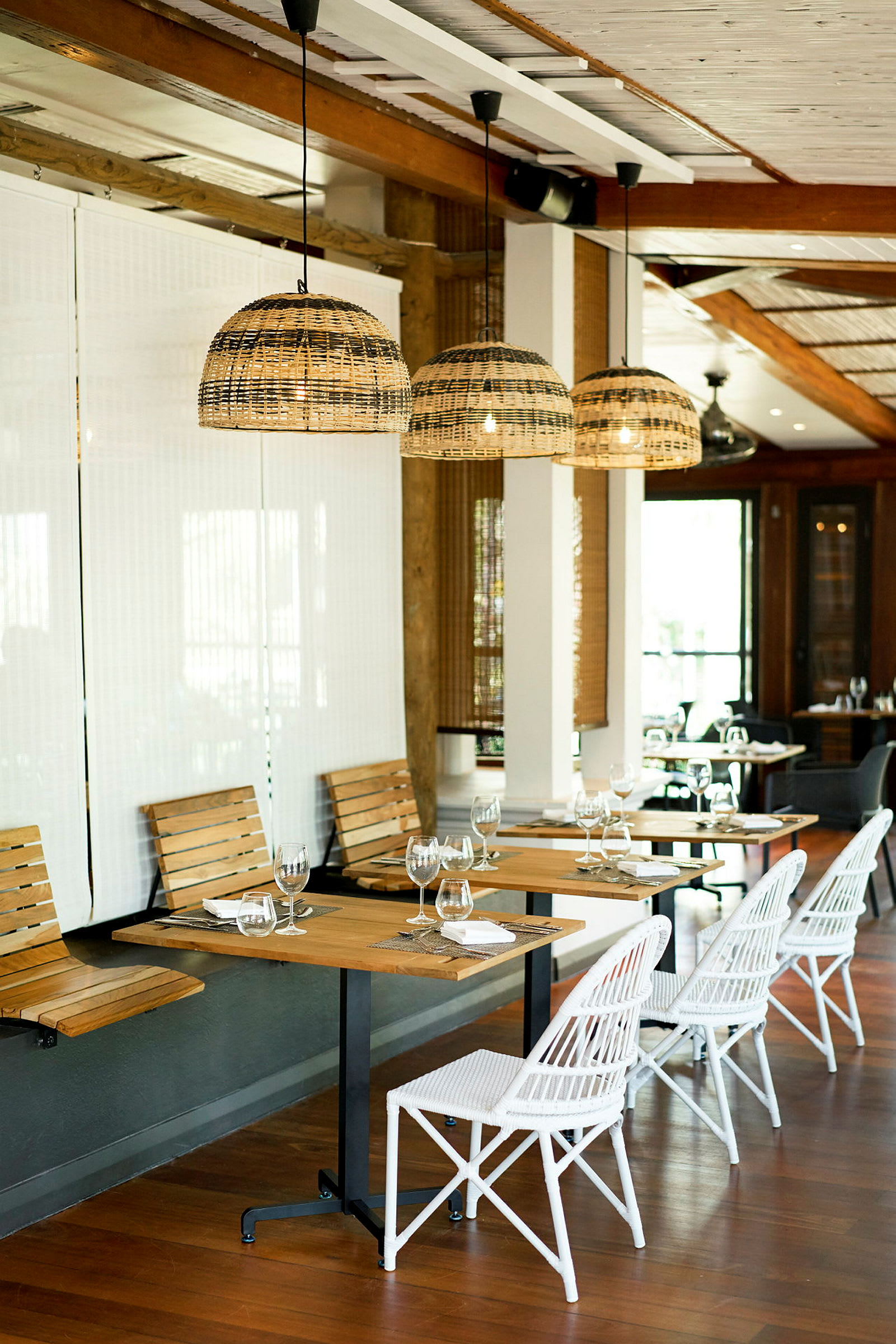 En restaurang med träbord, vita stolar och hängande lampor av rotting. (AI-genererad text)