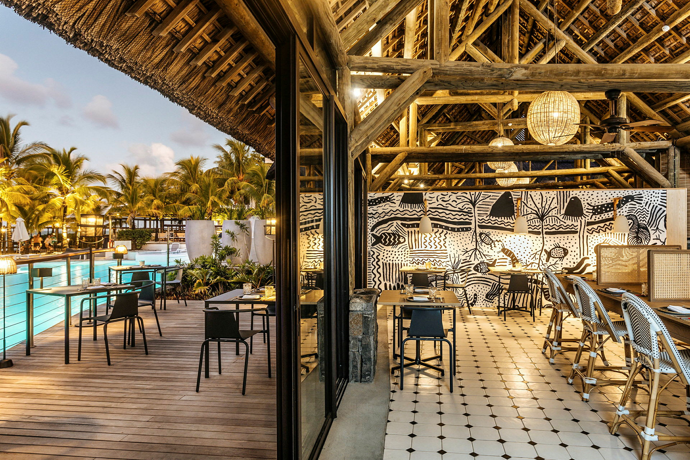 En restaurang med öppen sittplats, med modern design och pool samt palmer synliga i bakgrunden. (AI-genererad text)