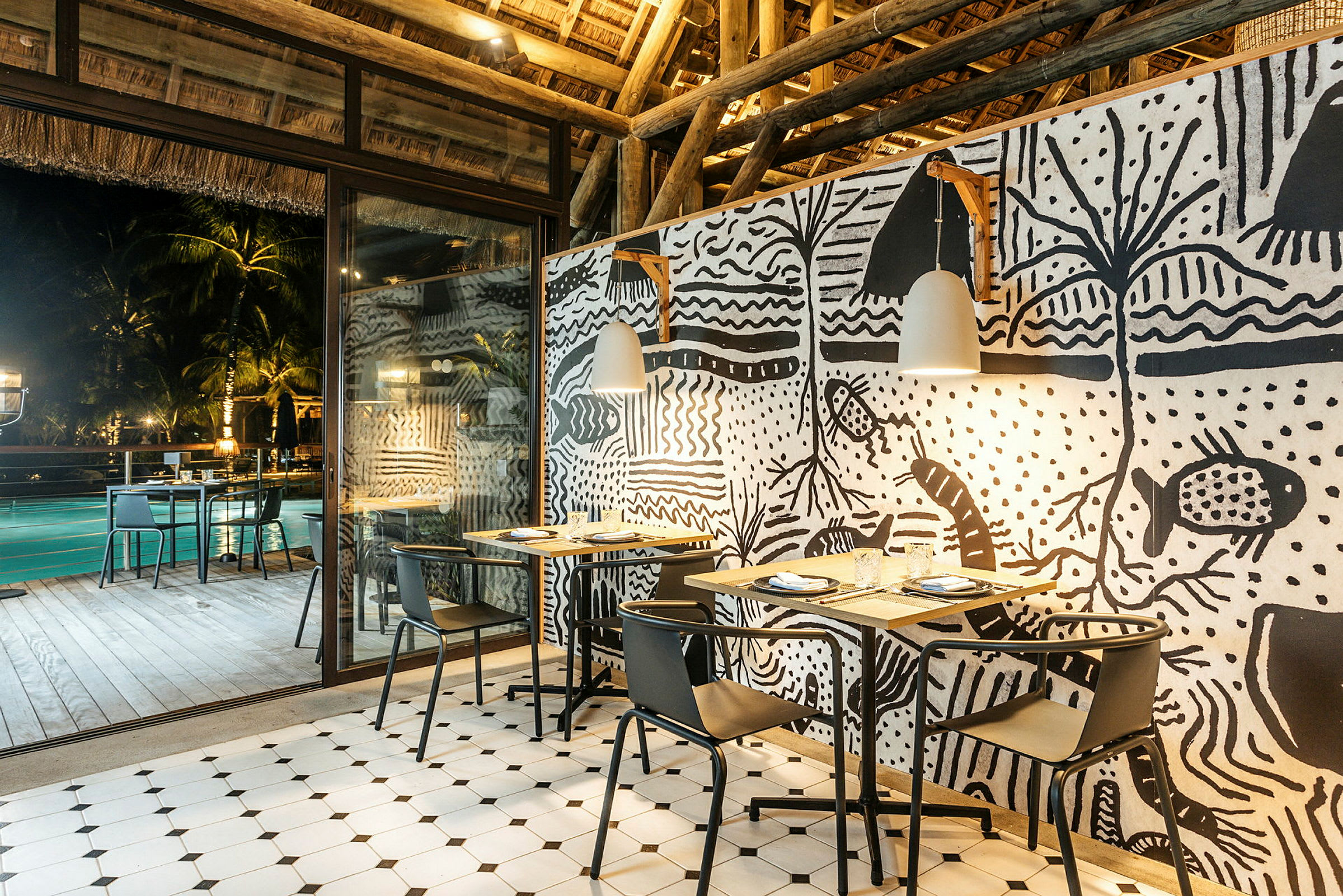 En restaurang med dekorativa väggar och belysning med bord och stolar uppställda. (AI-genererad text)