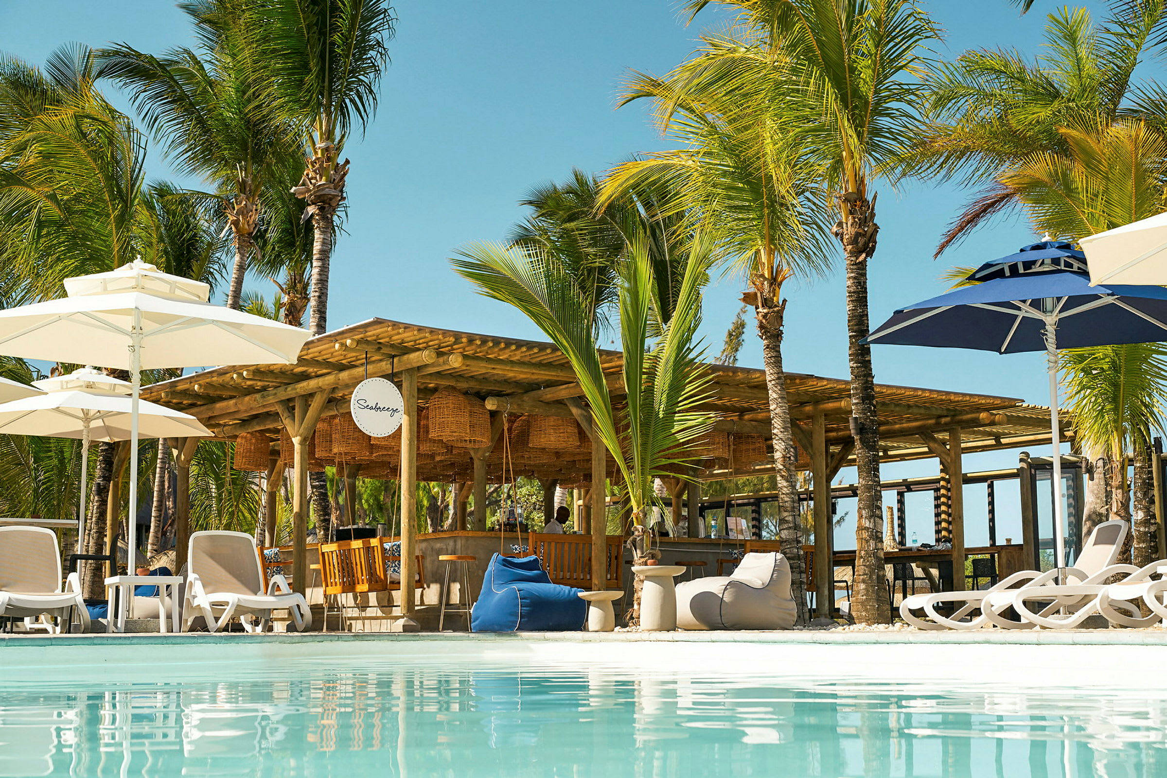 Ett poolområde med solstolar, parasoller och en strandbar omgiven av palmer. (AI-genererad text)