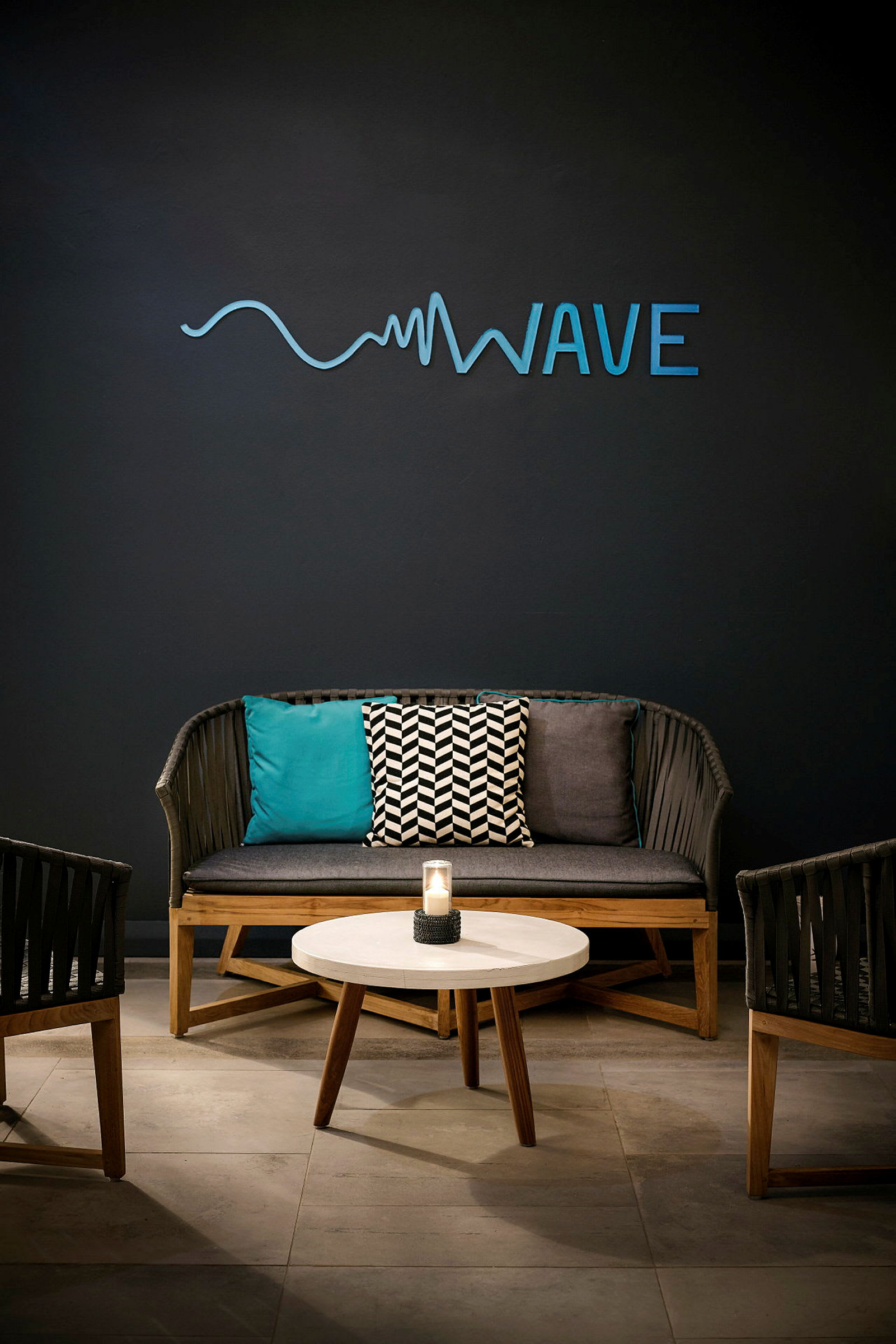 En sittgrupp med en soffa, två stolar, ett runt bord och en vägg med texten 'Wave'. (AI-genererad text)