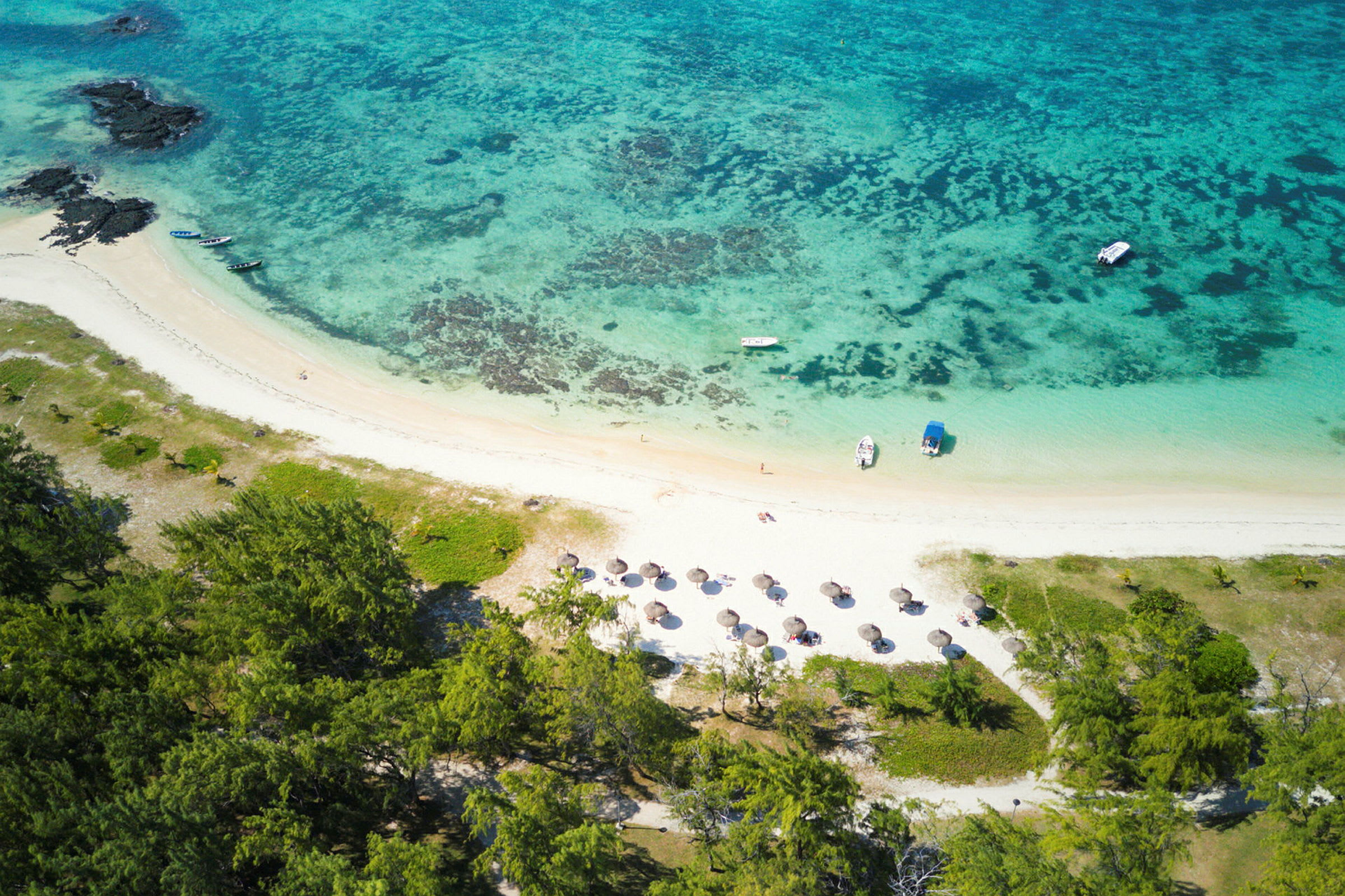 Flygbild av en tropisk strand med parasoller, båtar och omgivande grönska. (AI-genererad text)