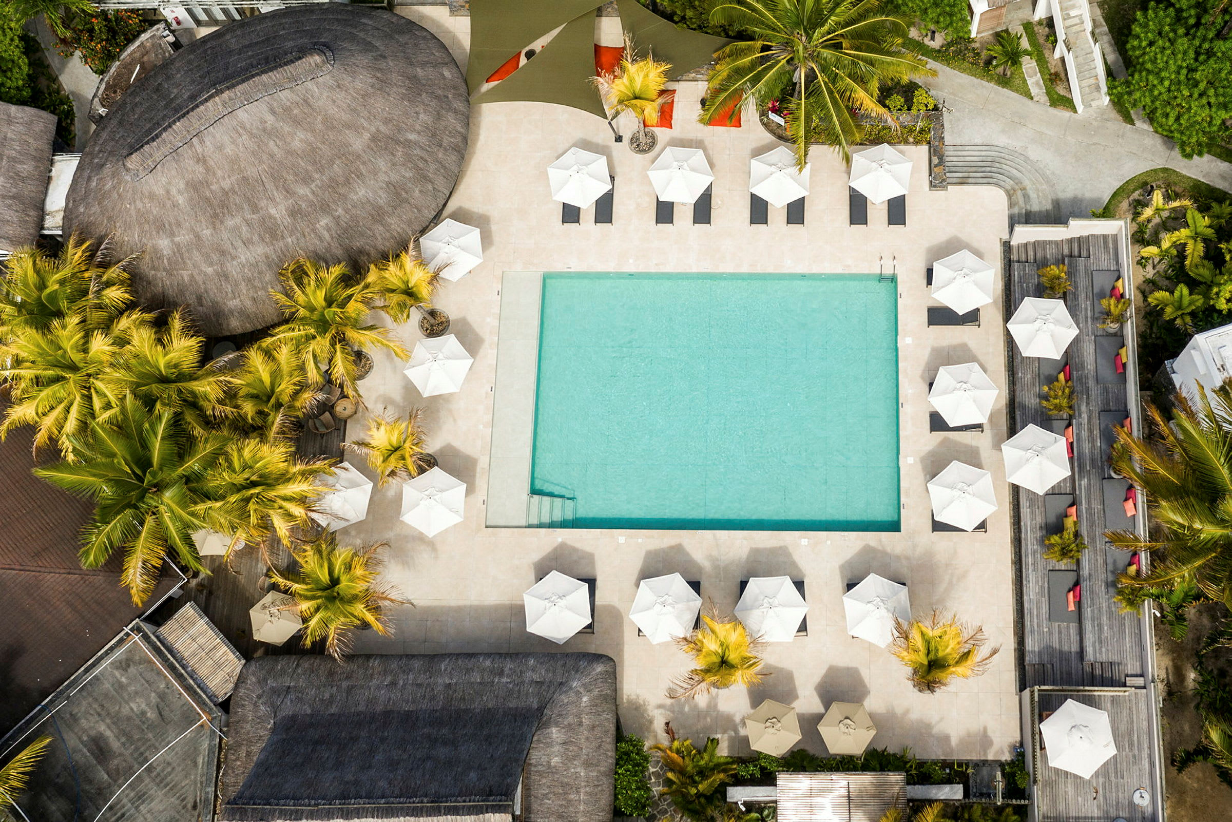Flygfoto av en strandnära hotellpool omgiven av parasoller och solsängar. (AI-genererad text)