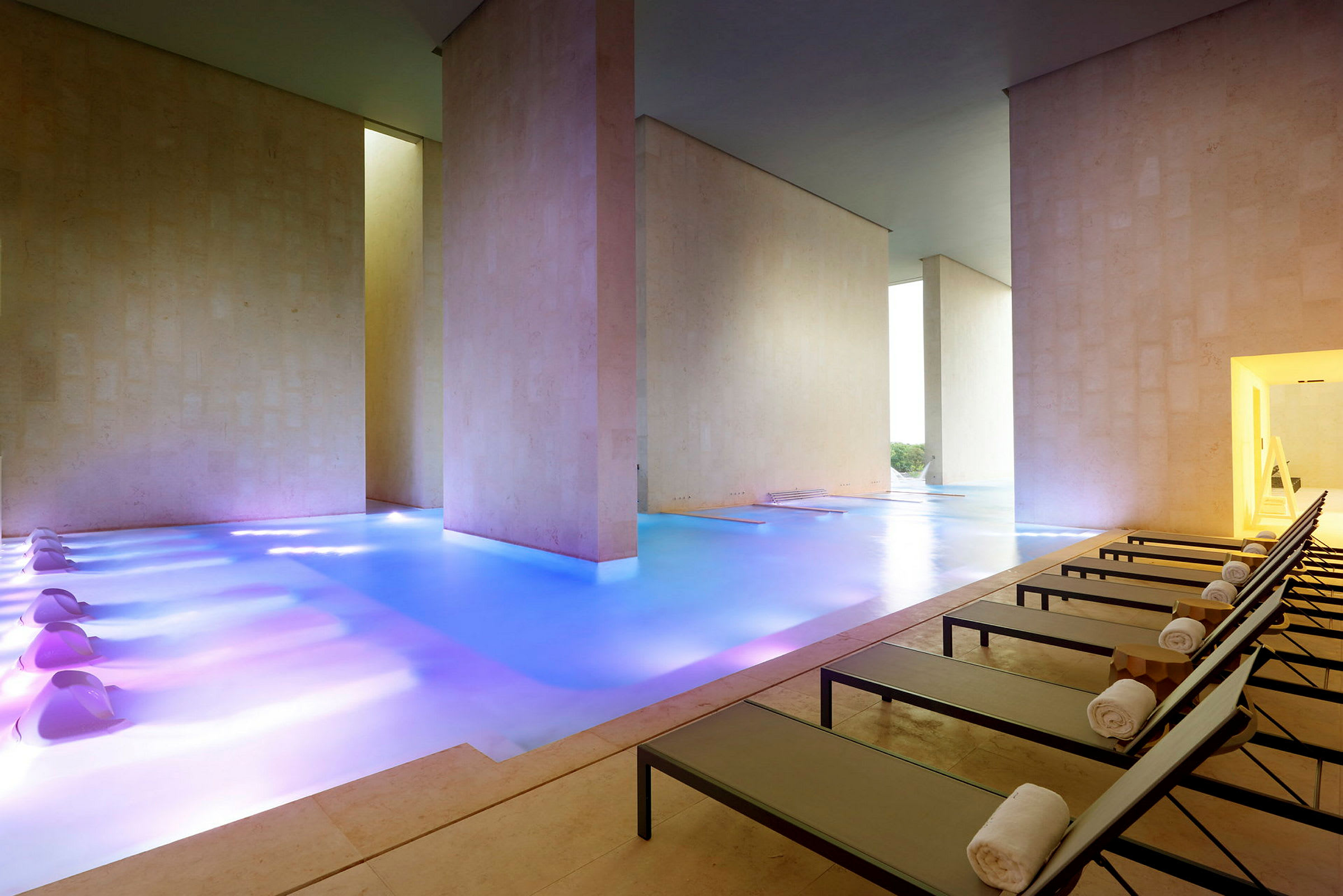 Ett elegant inomhusspa med en uppvärmd pool i en modern miljö och resårstolar längs ena sidan. (AI-genererad text)