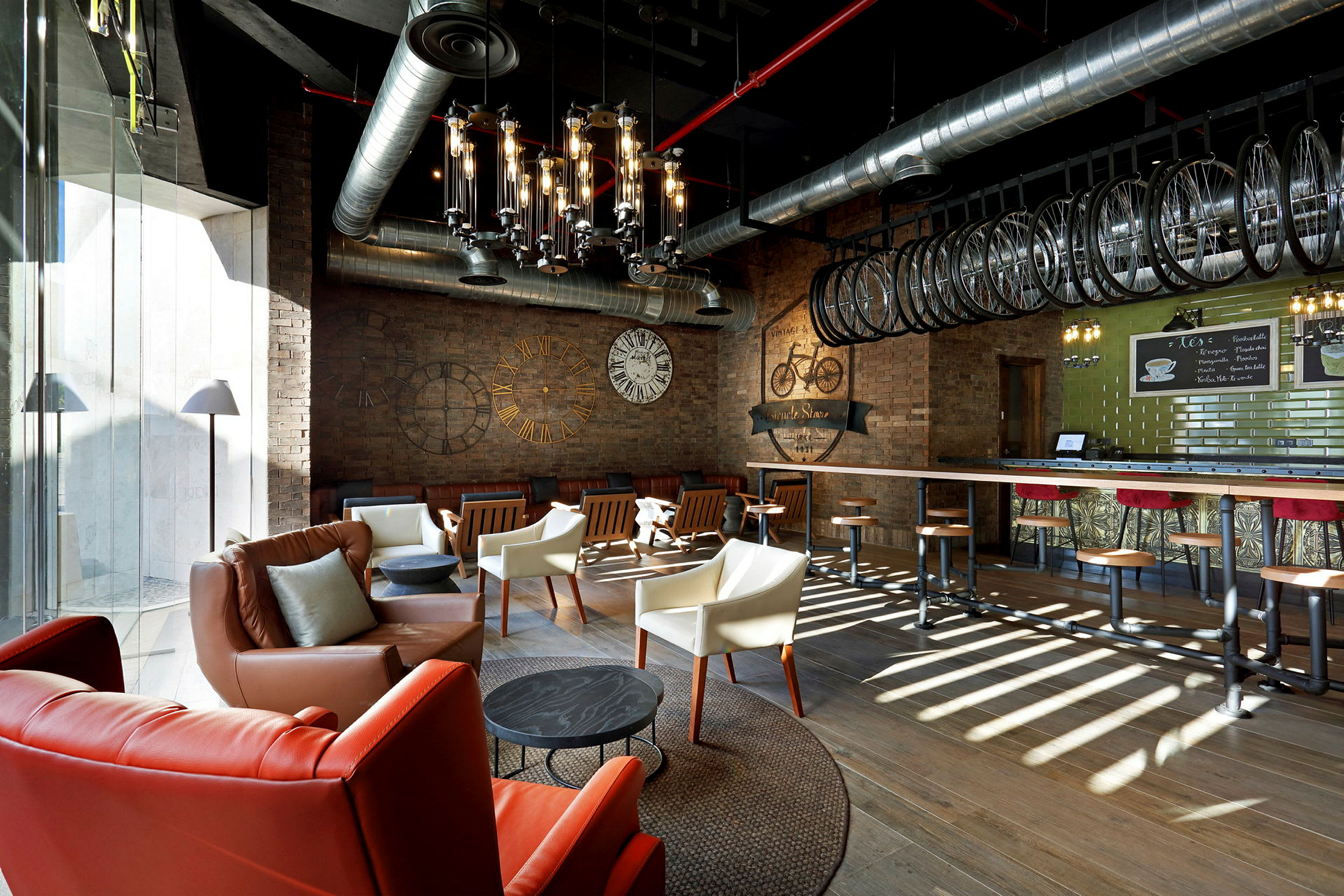 En interiör av en modern kaffebar med möblerade sittplatser, synliga ventilationsrör och ett industriellt designtema. (AI-genererad text)