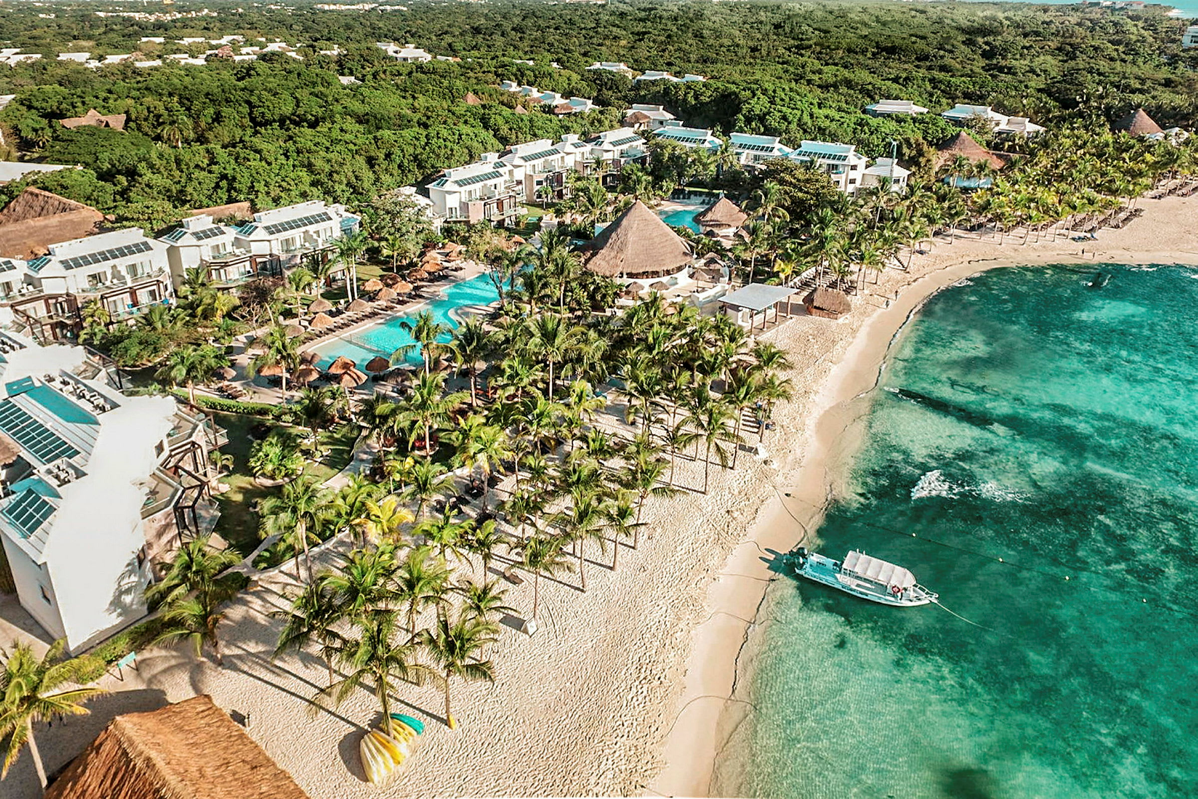 Hotellområde med pooler och trädgårdar vid en sandstrand med turkost vatten. (AI-genererad text)