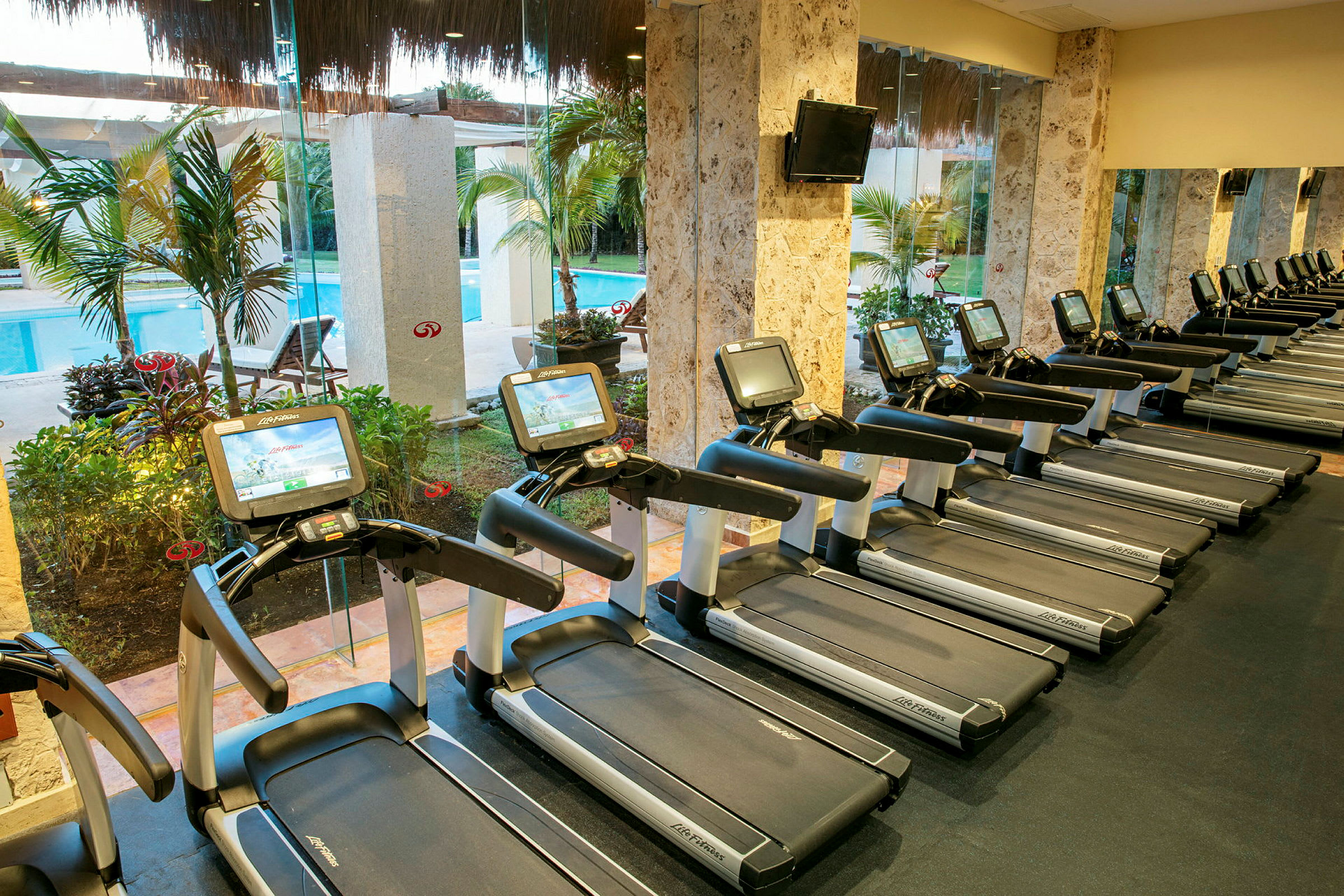 En rad löpband i ett gym med glasväggar som vetter mot en pool utomhus. (AI-genererad text)
