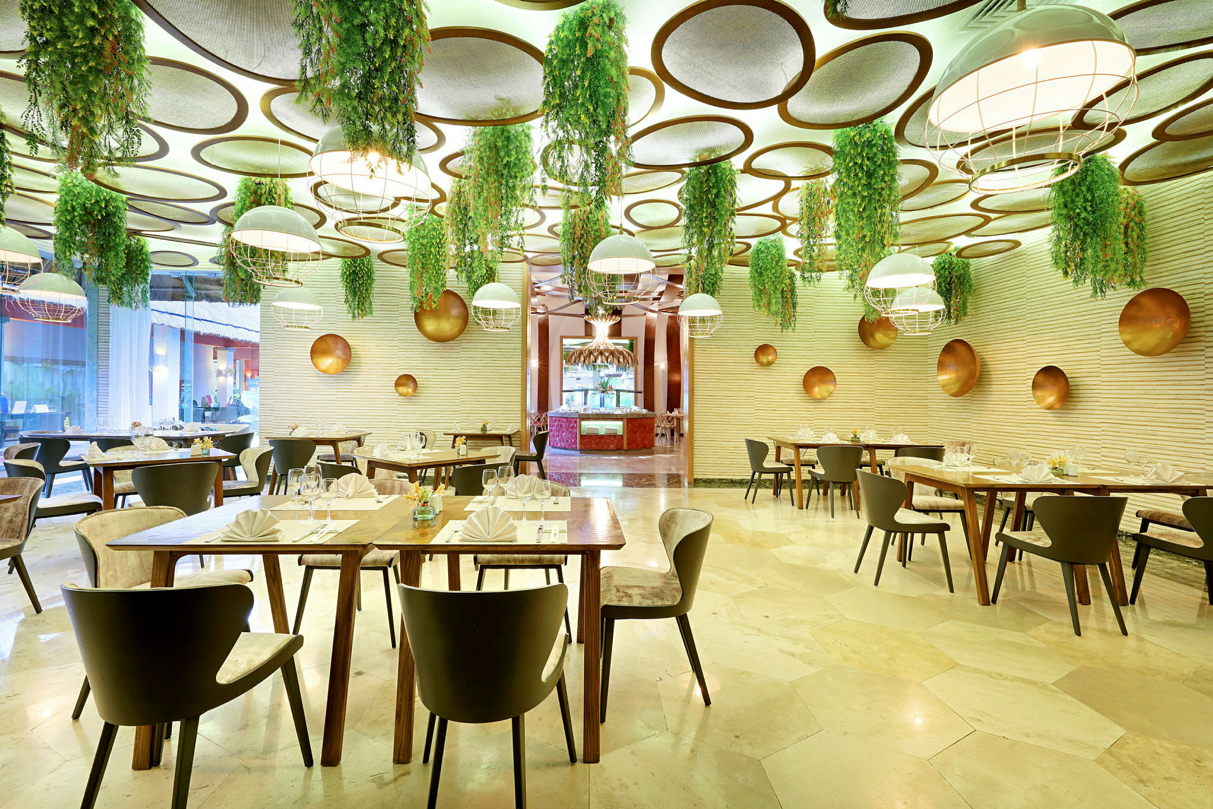 En restaurang med modern inredning, där taket är dekorerat med hängande gröna växter och runda paneler. Matsalsmöbler är stilrena och borden är dukade. (AI-genererad text)