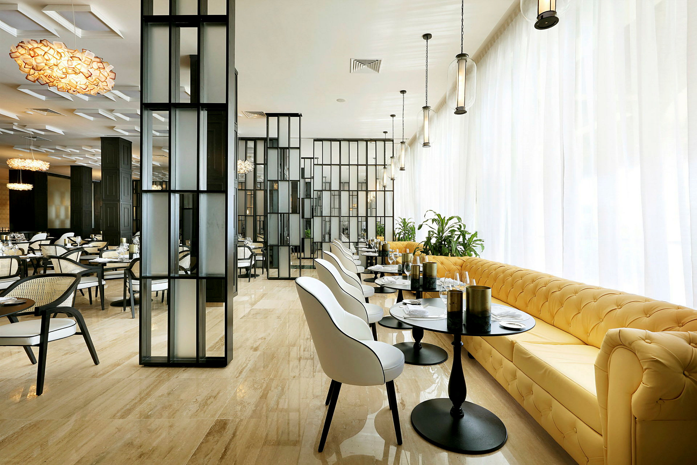 Ett modernt restaurangområde med stilren inredning, vita stolar, gula soffor, glasbord och stora glaspartier. (AI-genererad text)