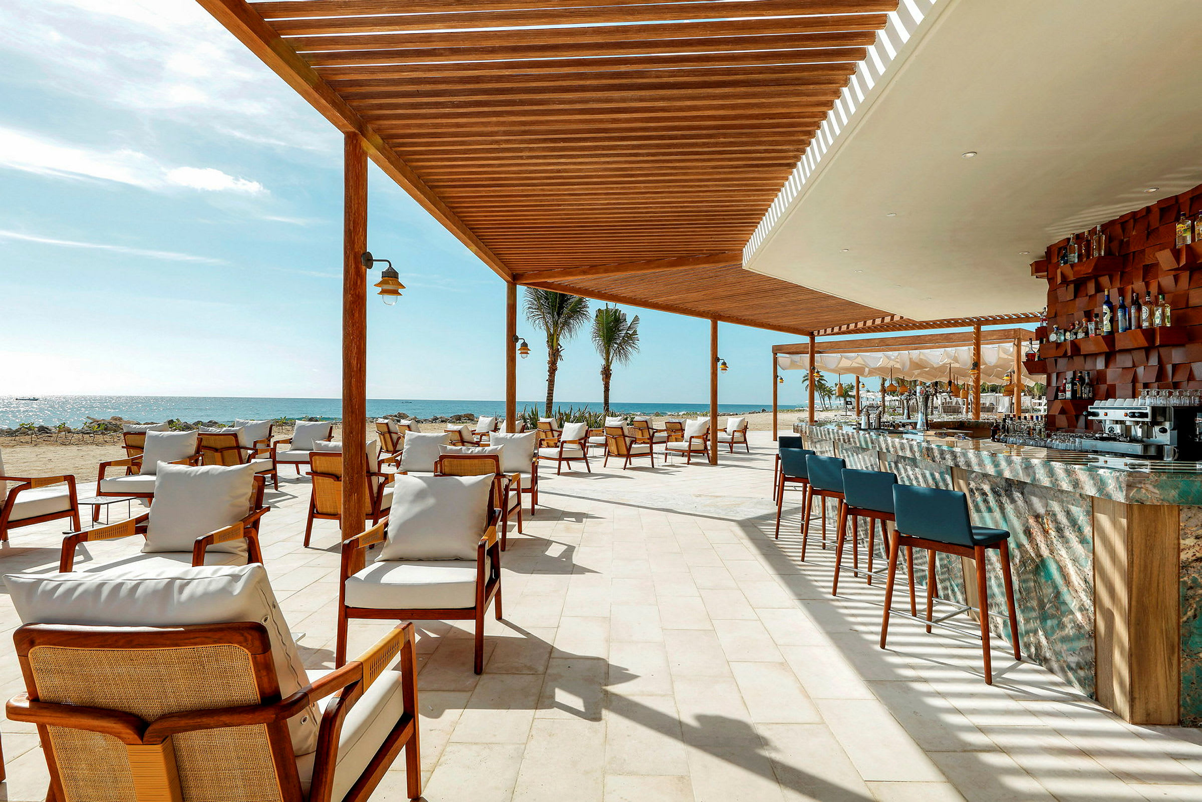 En utomhusrestaurang med sittplatser och en bar under en träpaviljong vid stranden. (AI-genererad text)