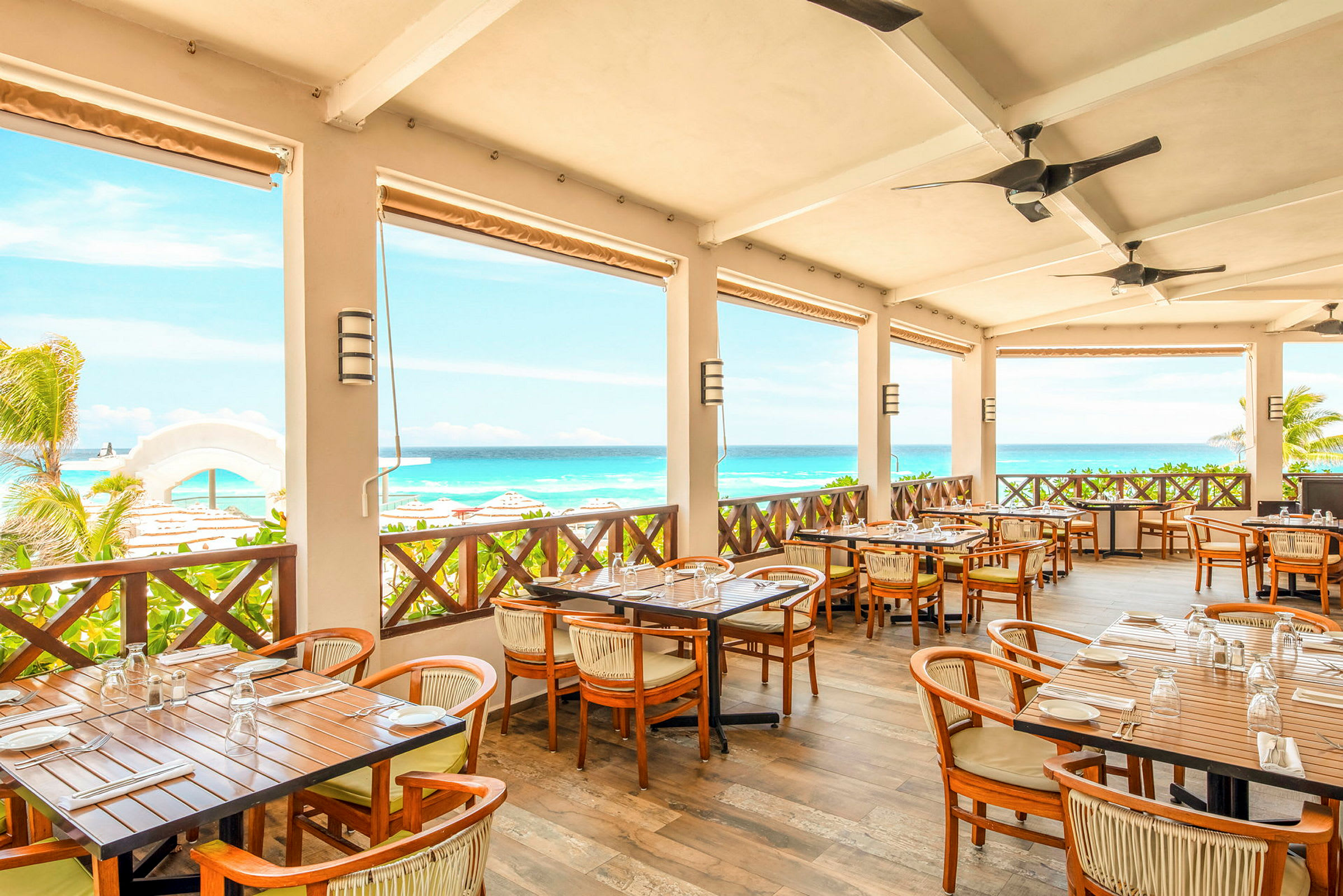 Restaurang med terrass som har bord och stolar, utsikt över havet och stranden. (AI-genererad text)