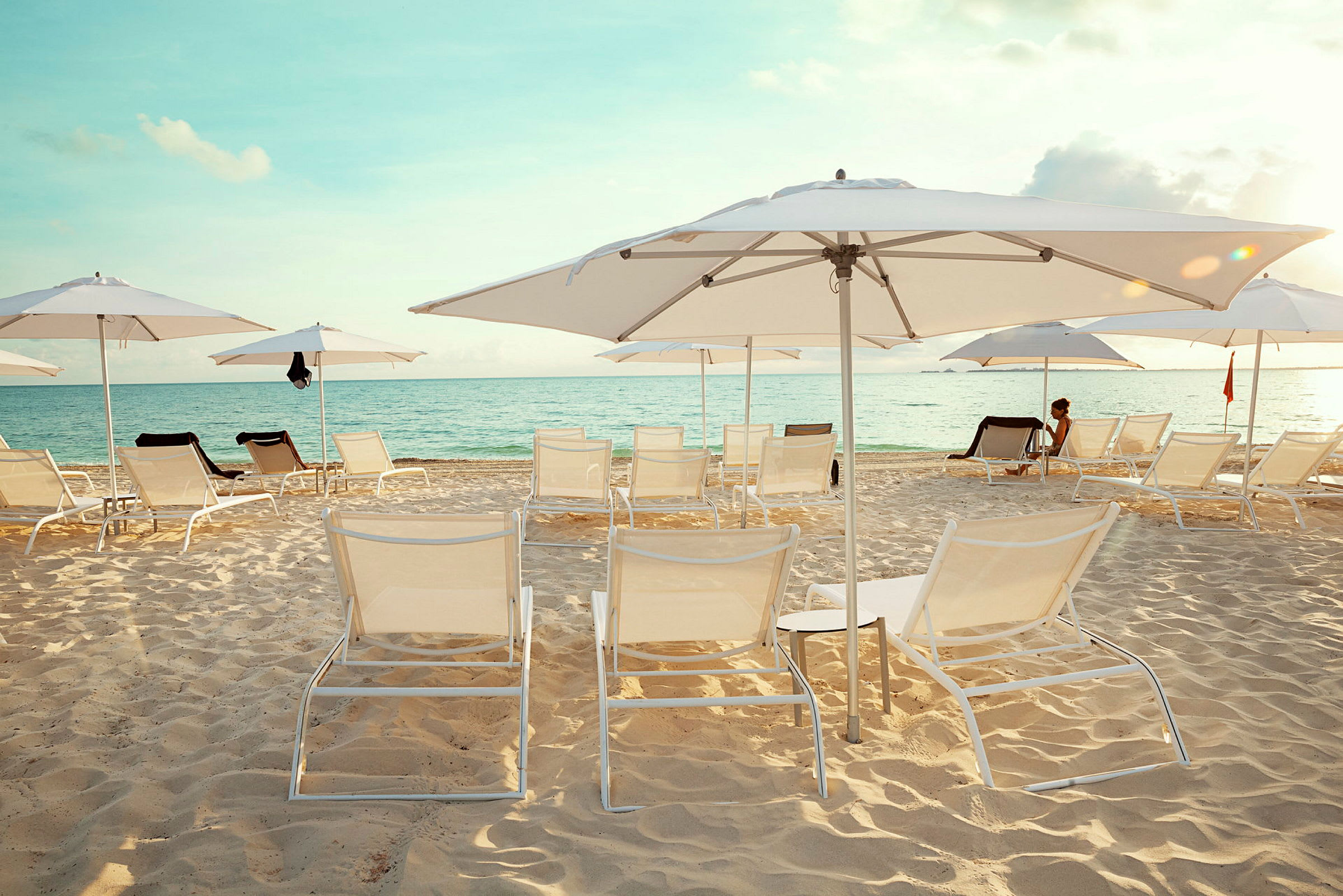 Bild av en strand med solstolar och parasoller uppställda på sanden, med utsikt över havet. (AI-genererad text)