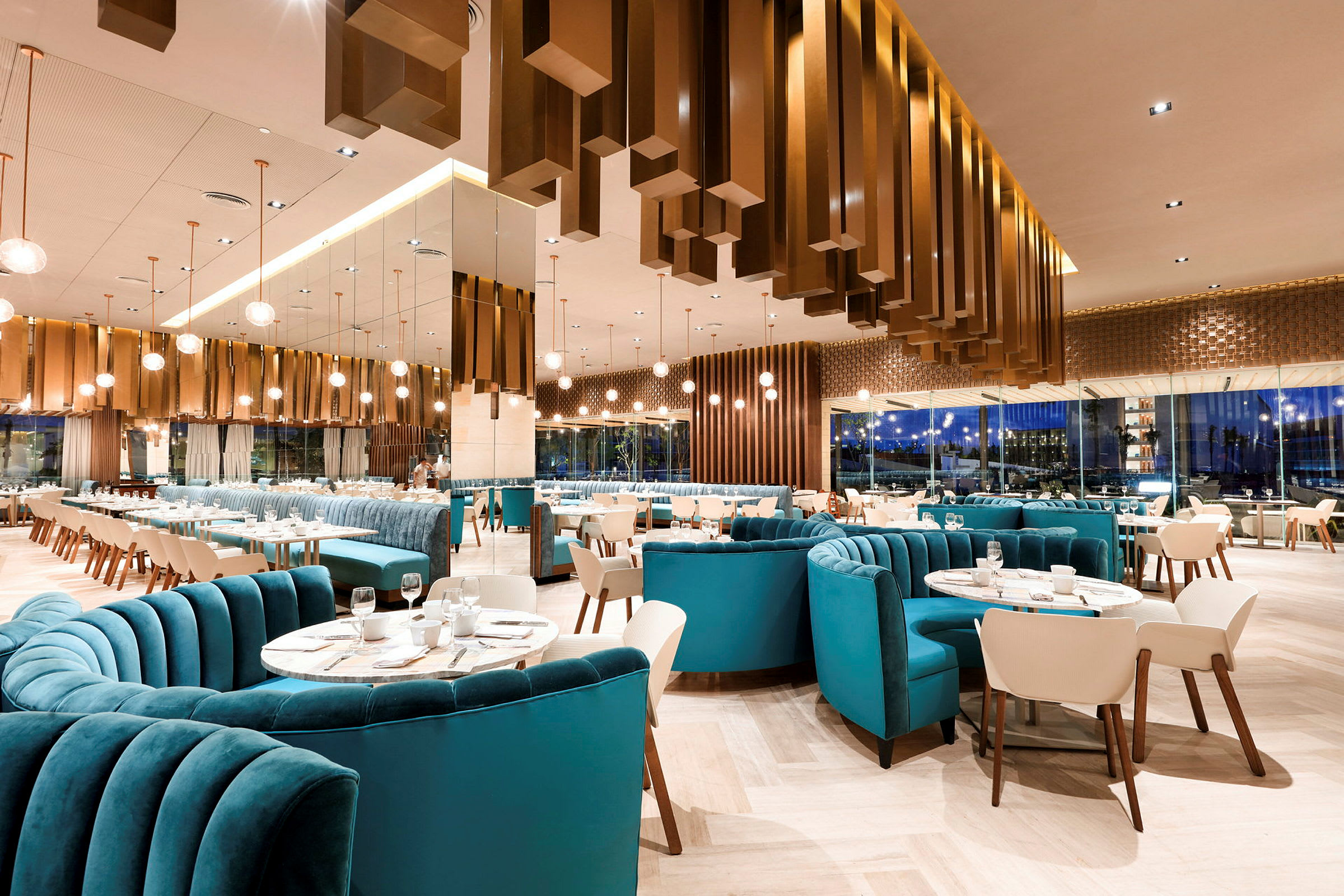 En modern restaurang med eleganta möbler, blå vadderade soffor och vita stolar, samt tallrikar och vinglas placerade på borden. (AI-genererad text)