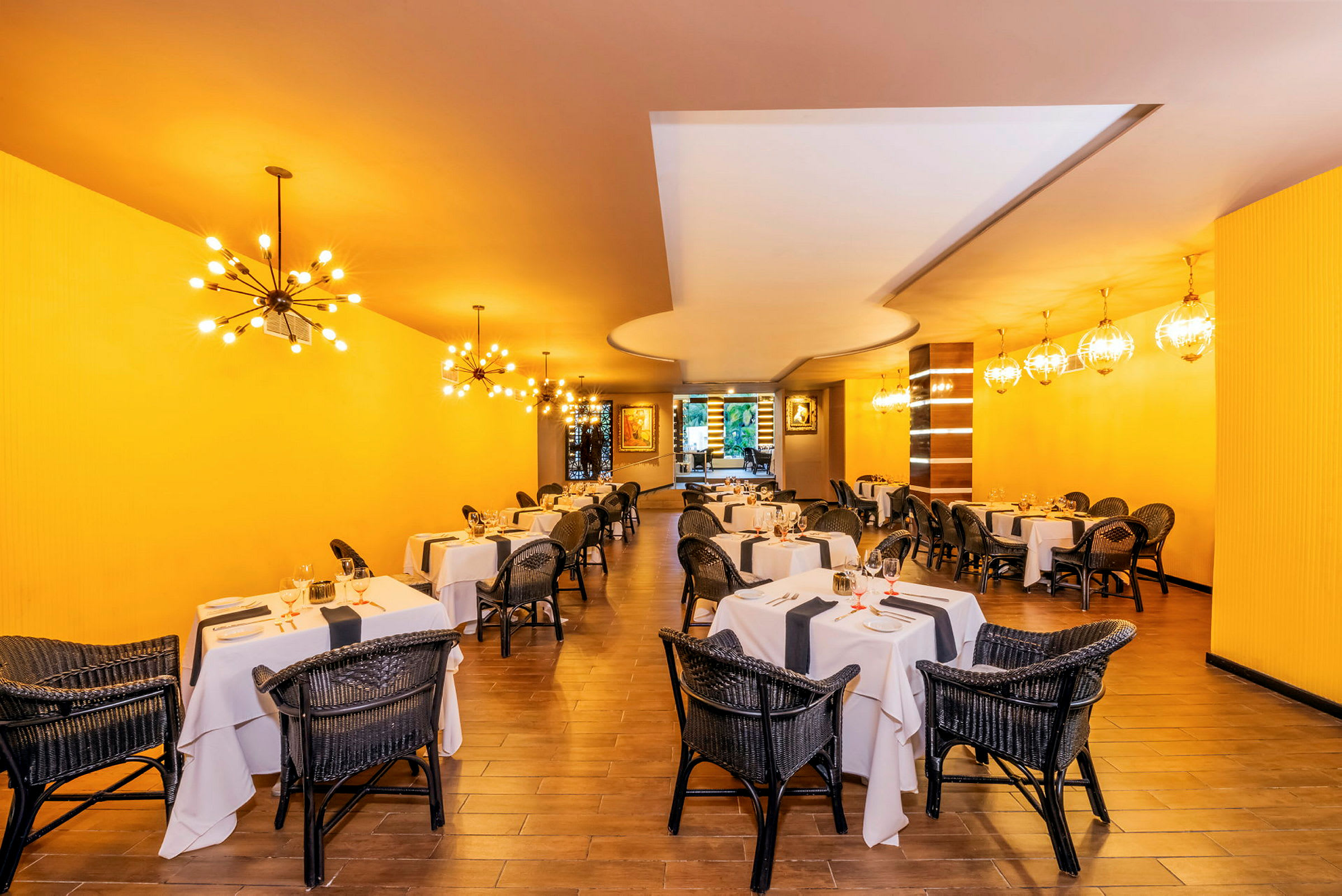 Restaurang med dukade bord och rottingstolar, gul vägg och dekorativa lampor. (AI-genererad text)