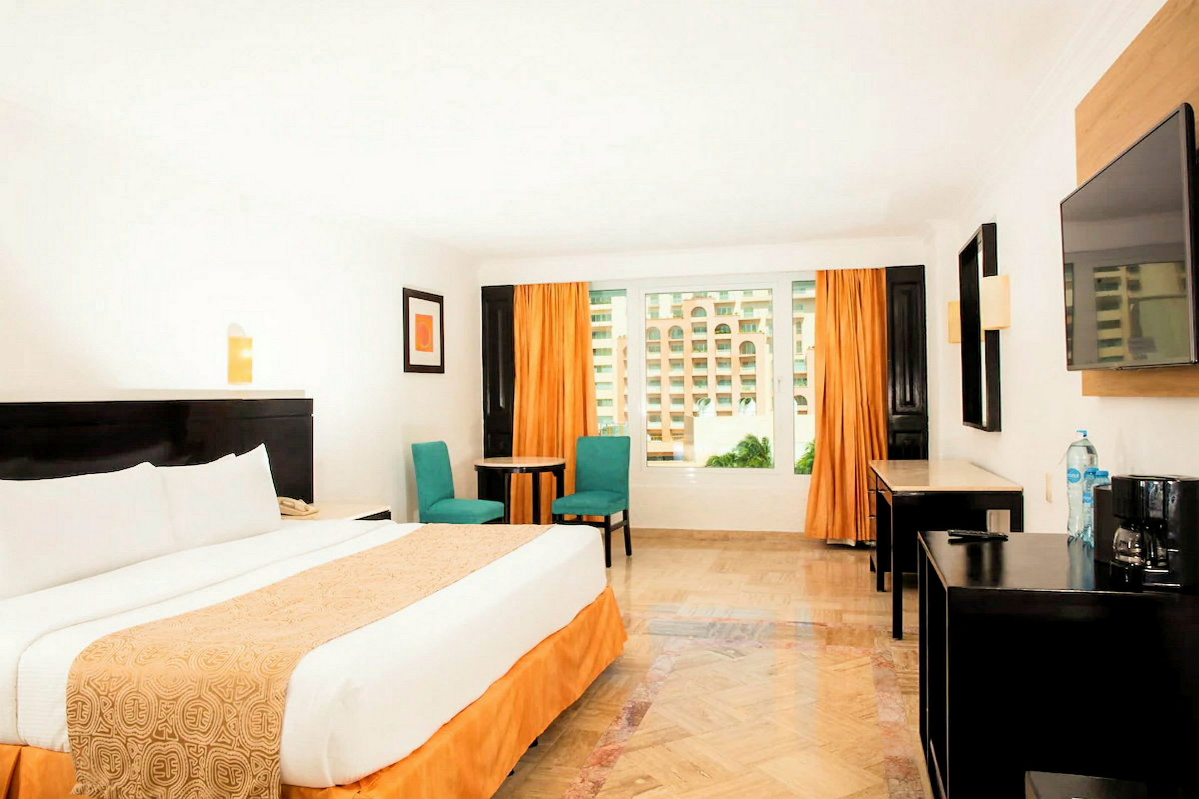 Ett hotellrum med en stor säng, två stolar, ett bord och fönster med orange gardiner. (AI-genererad text)
