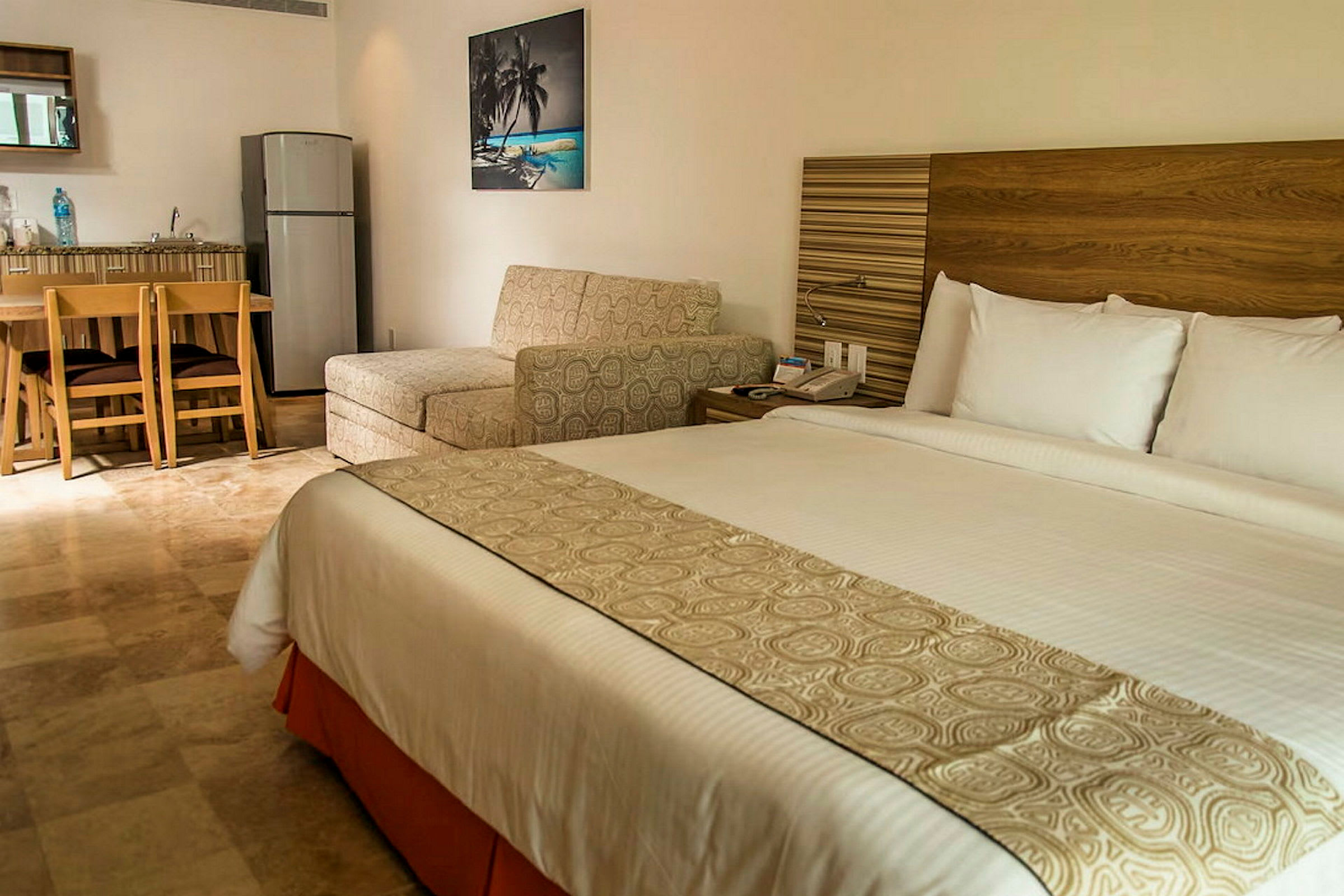 Ett hotellrum med en stor säng, sittmöbler, bord och ett litet kök med kylskåp. (AI-genererad text)