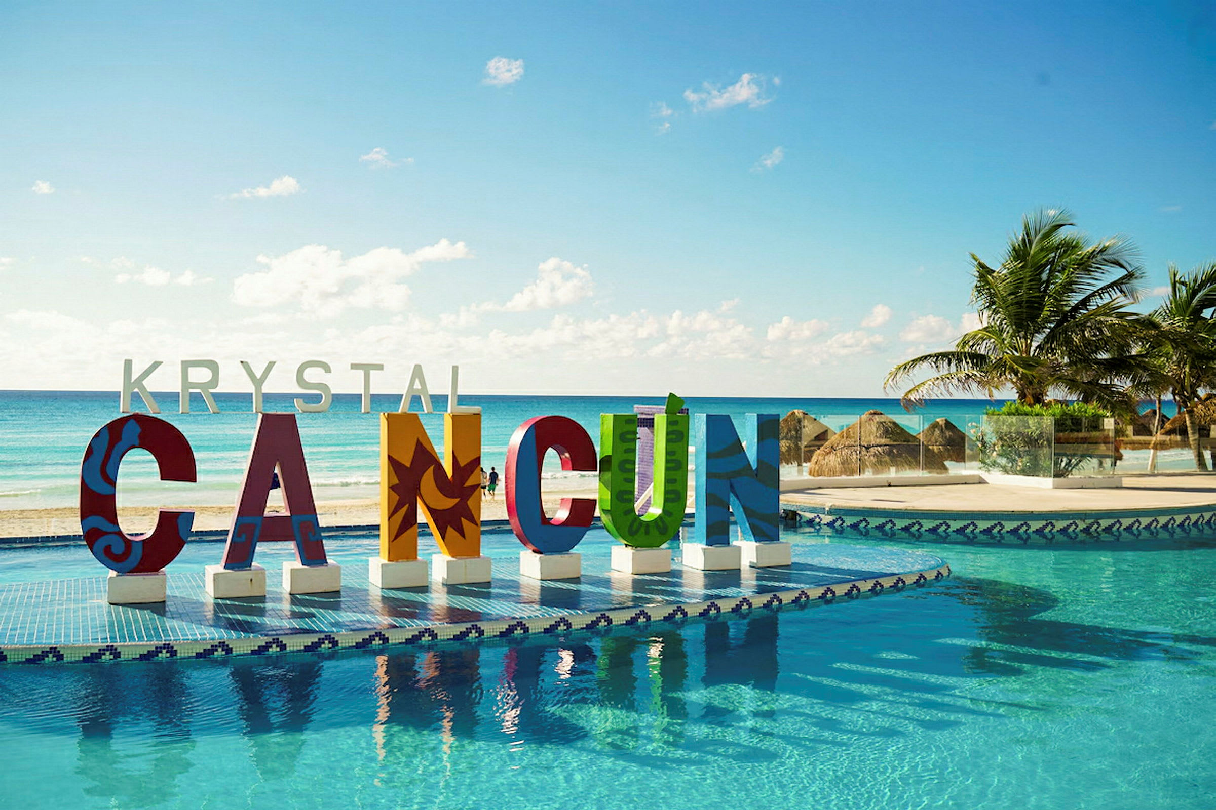 Färgglada bokstäver som bildar ordet 'CANCUN' vid en pool med havsutsikt och palmer. (AI-genererad text)