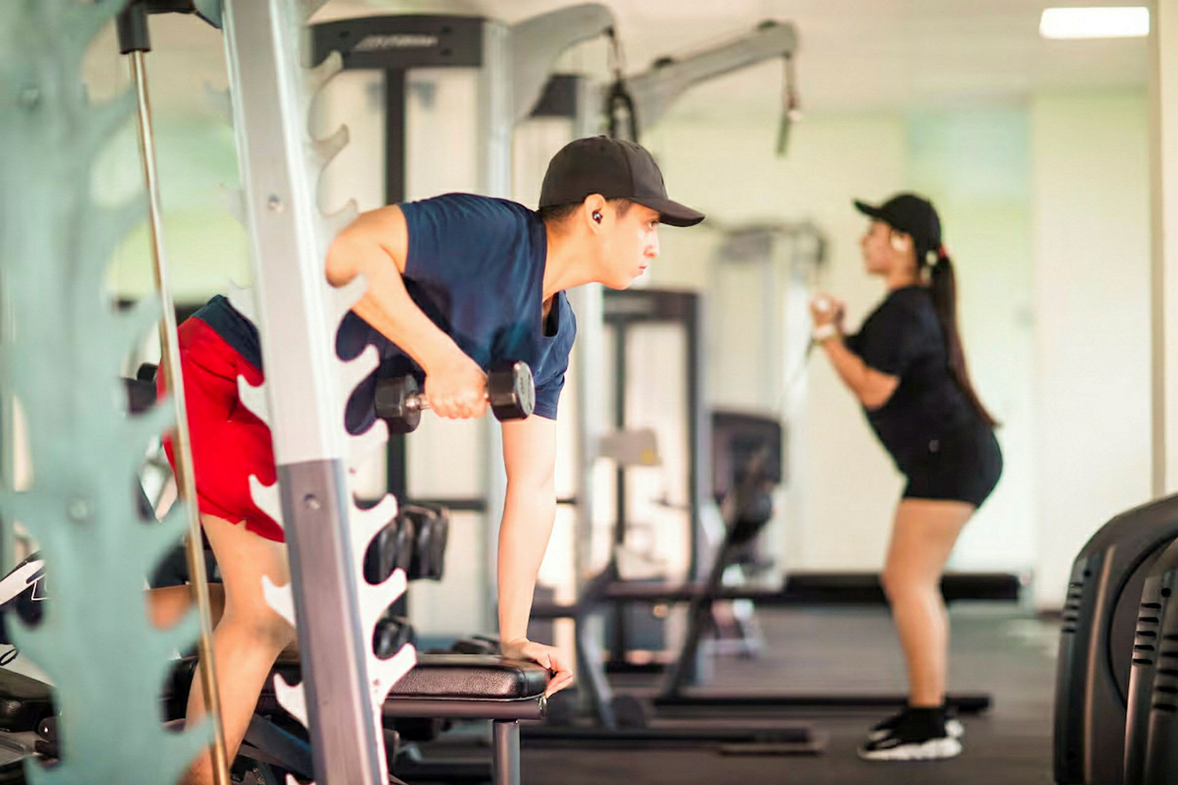 Två personer tränar i ett gym, där den ena använder hantlar och den andra en kabelmaskin. (AI-genererad text)