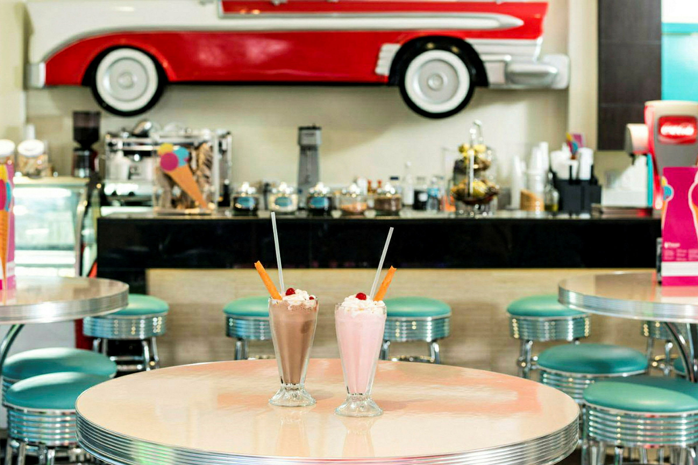 Bild på ett inomhuskafé med en retrostil, bord och stolar samt milkshakes i fokus. (AI-genererad text)