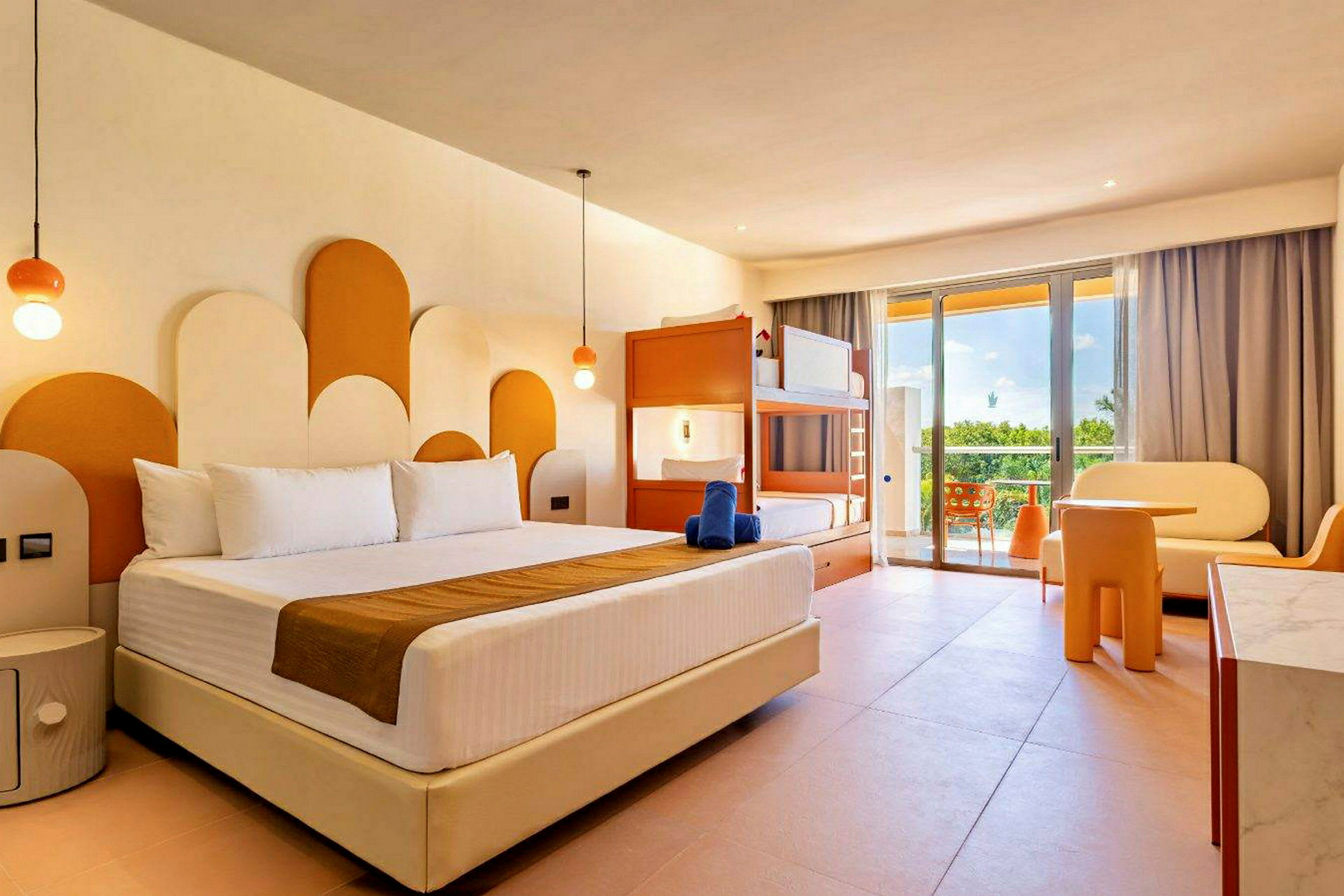 Ett hotellrum med en stor säng och en våningssäng, modern inredning i vitt och orange samt stora glasdörrar som leder ut till en balkong med utsikt. (AI-genererad text)