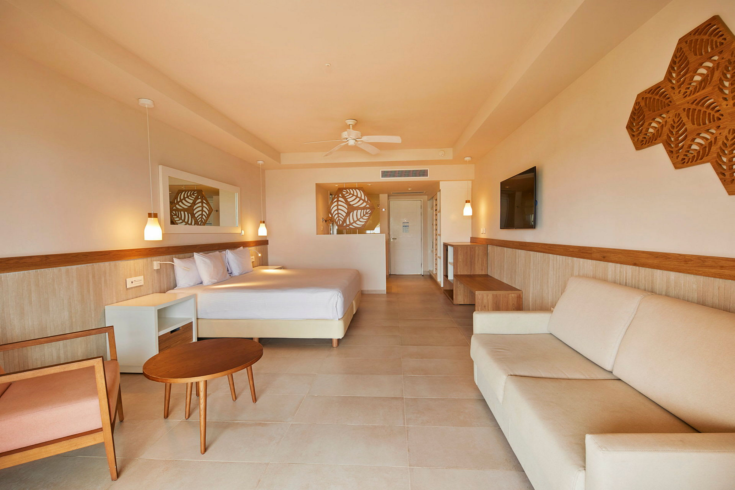 Hotellrum med ljus inredning, en säng, soffa och bord samt dekorativa väggdetaljer. (AI-genererad text)