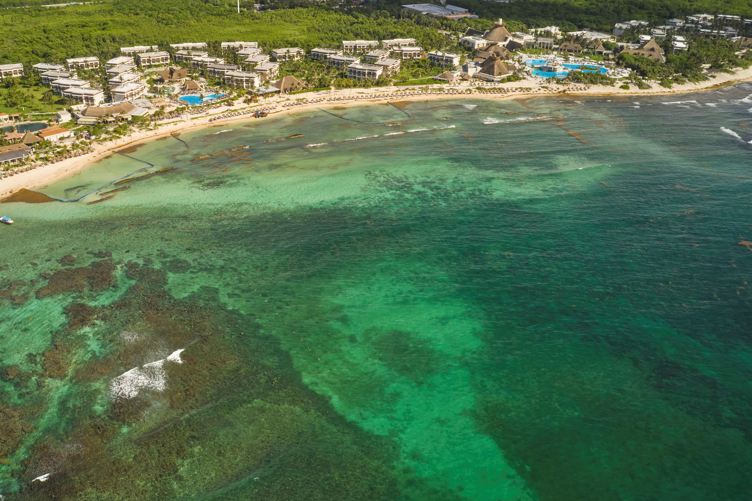Flygfoto av en kustlinje med en grönskande resorts omgiven av turkost hav och korallrev. (AI-genererad text)