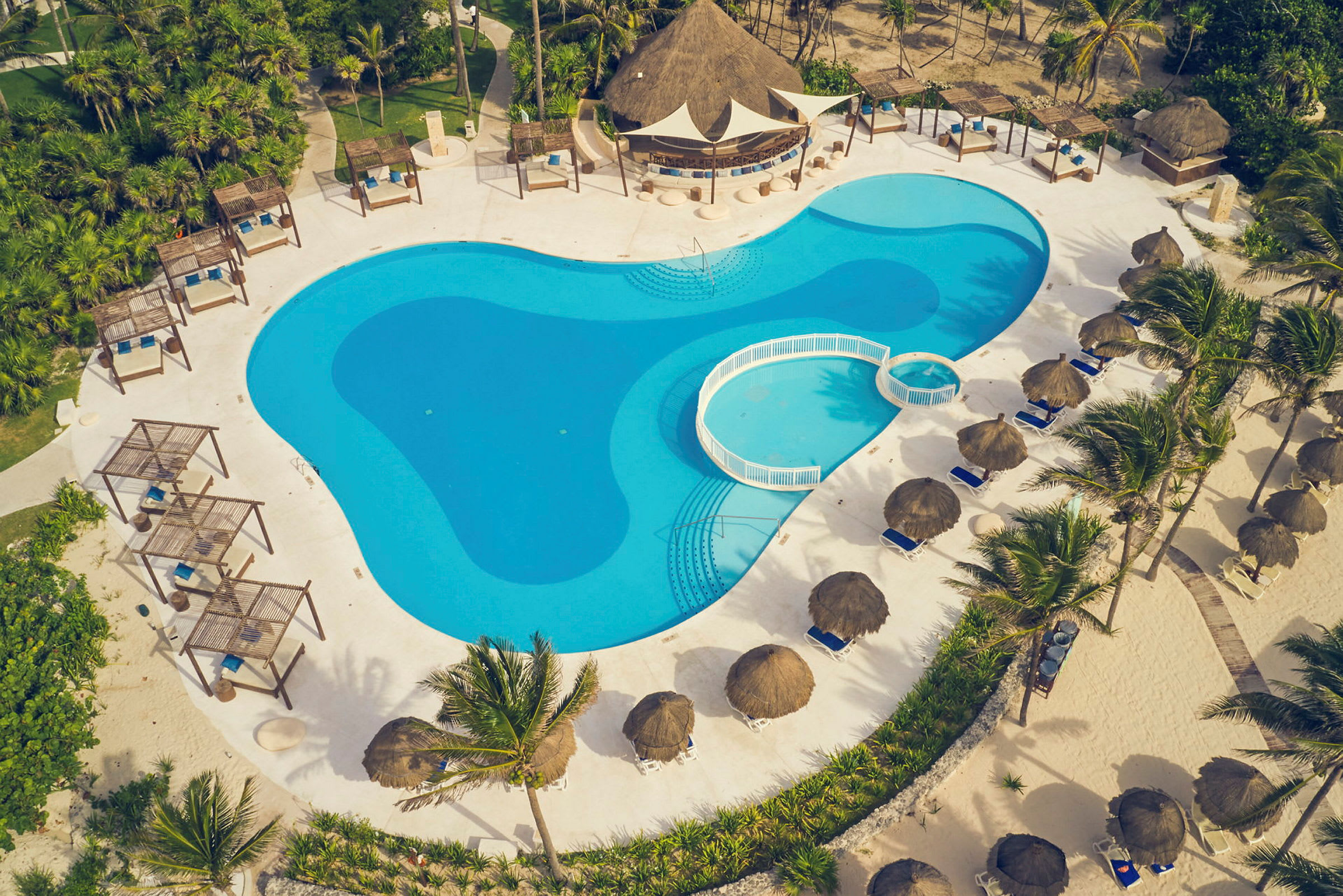 En stor swimmingpool omgiven av solstolar och parasoller, med grön vegetation runt omkring. (AI-genererad text)