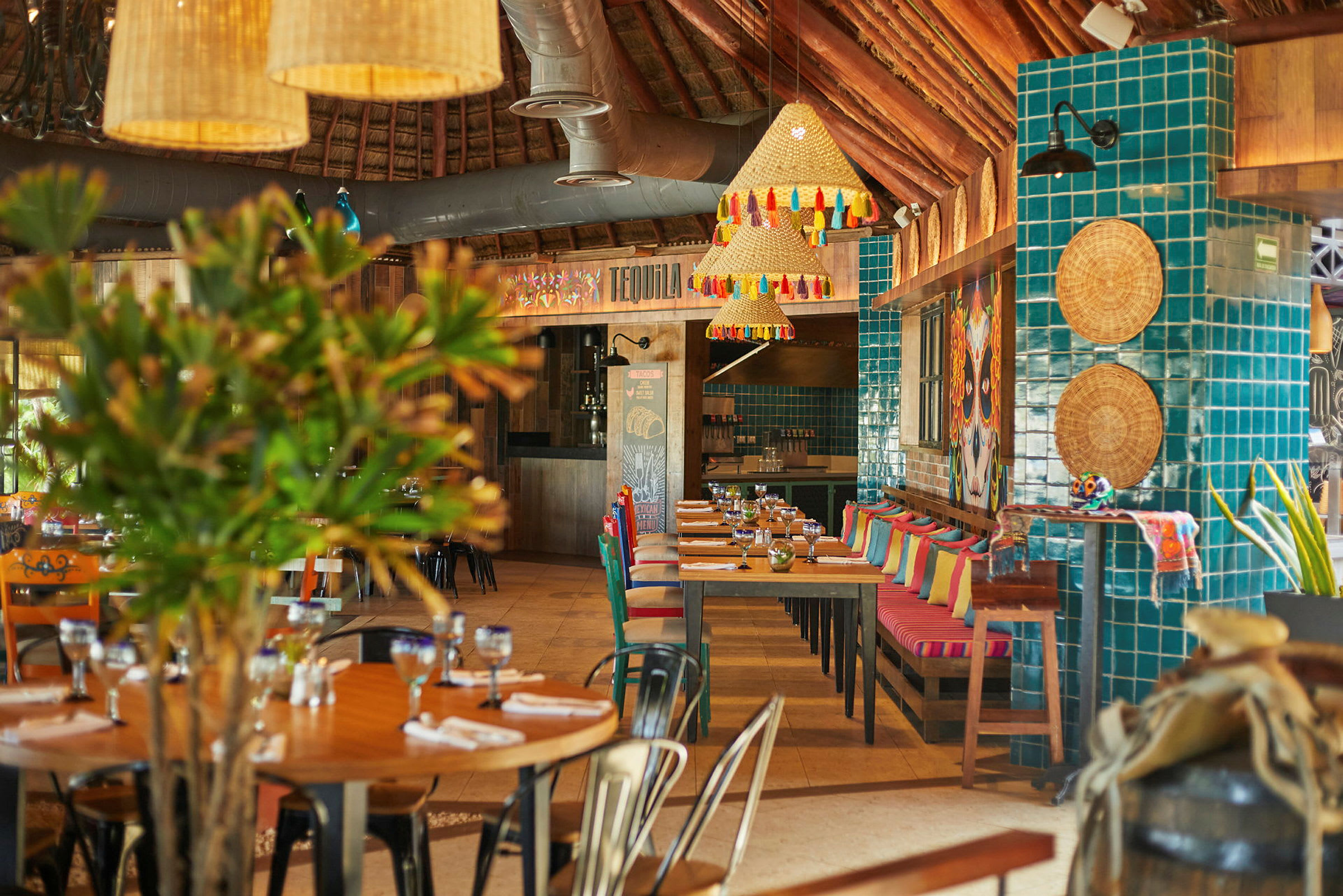 Ett färgglatt restauranginteriör med bord och stolar, dekorerna inkluderar kuddar, gröna växter och hängande lampor. (AI-genererad text)