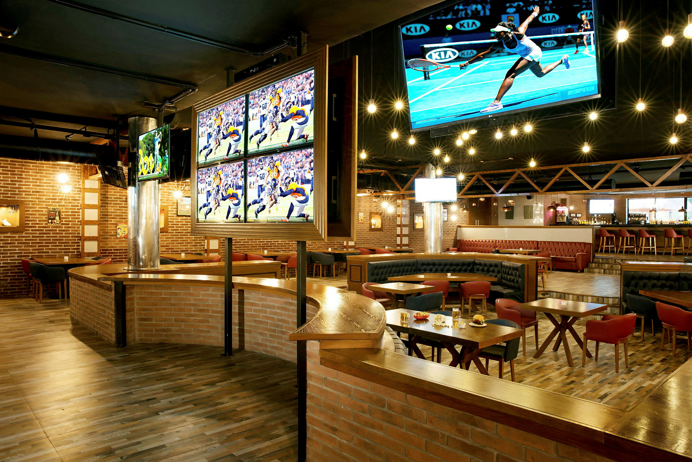 En sportbar med TV-skärmar som visar olika sportevenemang. Rummet har träbord, bekväma sittplatser och en bar i bakgrunden. (AI-genererad text)