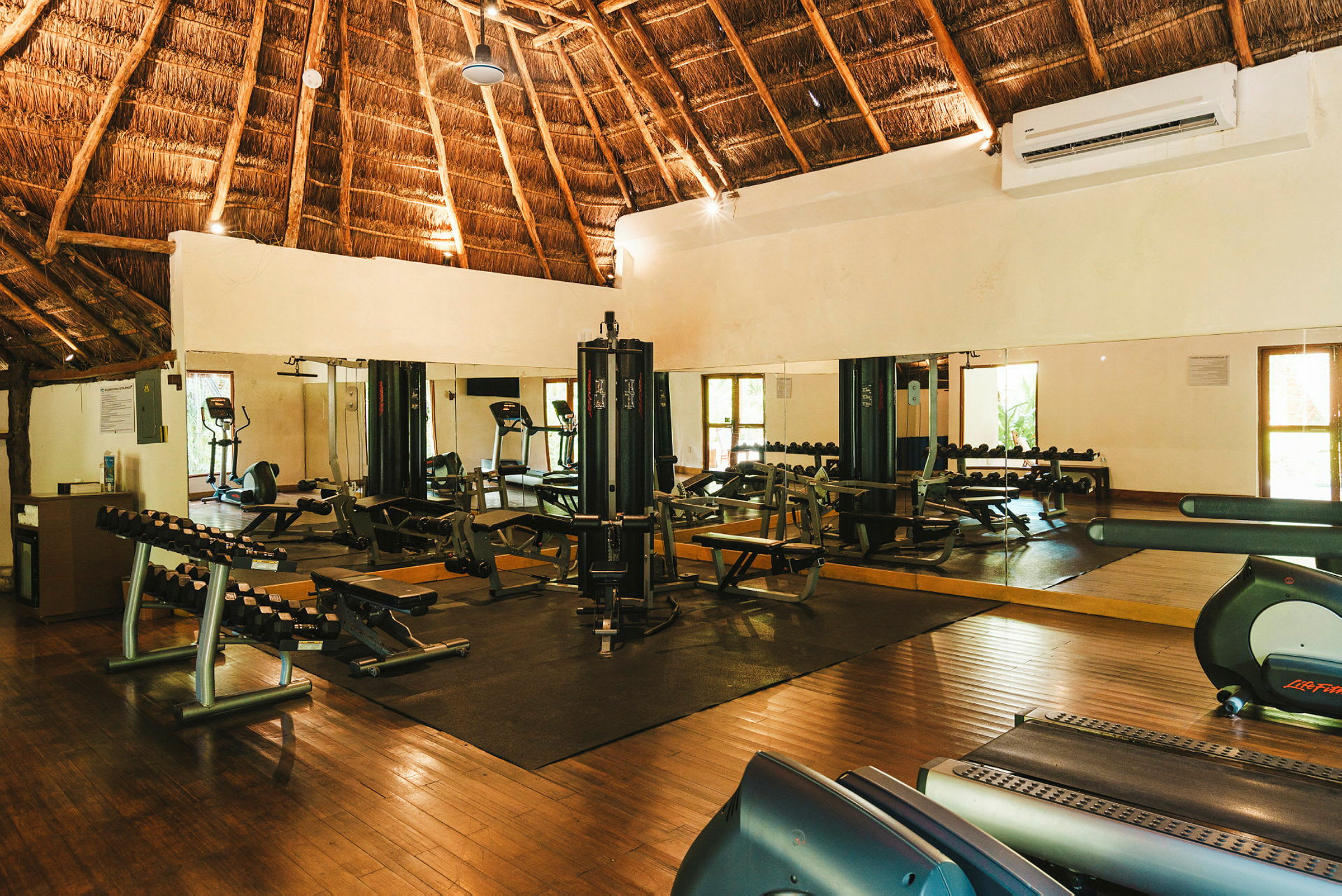 Ett gym med träningsutrustning som löpband, vikter och maskiner, i ett rum med tak av trä. (AI-genererad text)