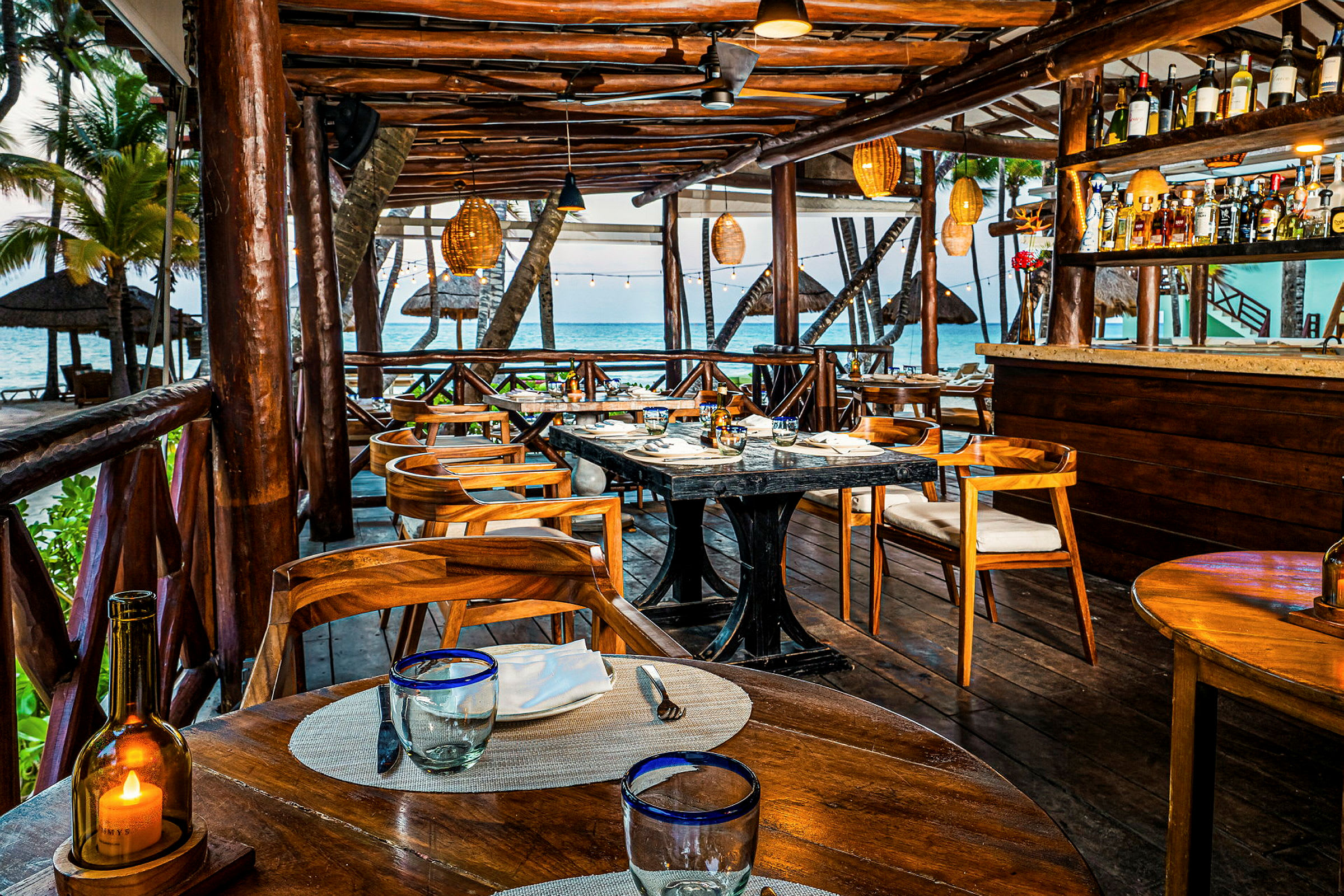 En strandnära restaurang med träinredning, bord och stolar, och havsutsikt. (AI-genererad text)