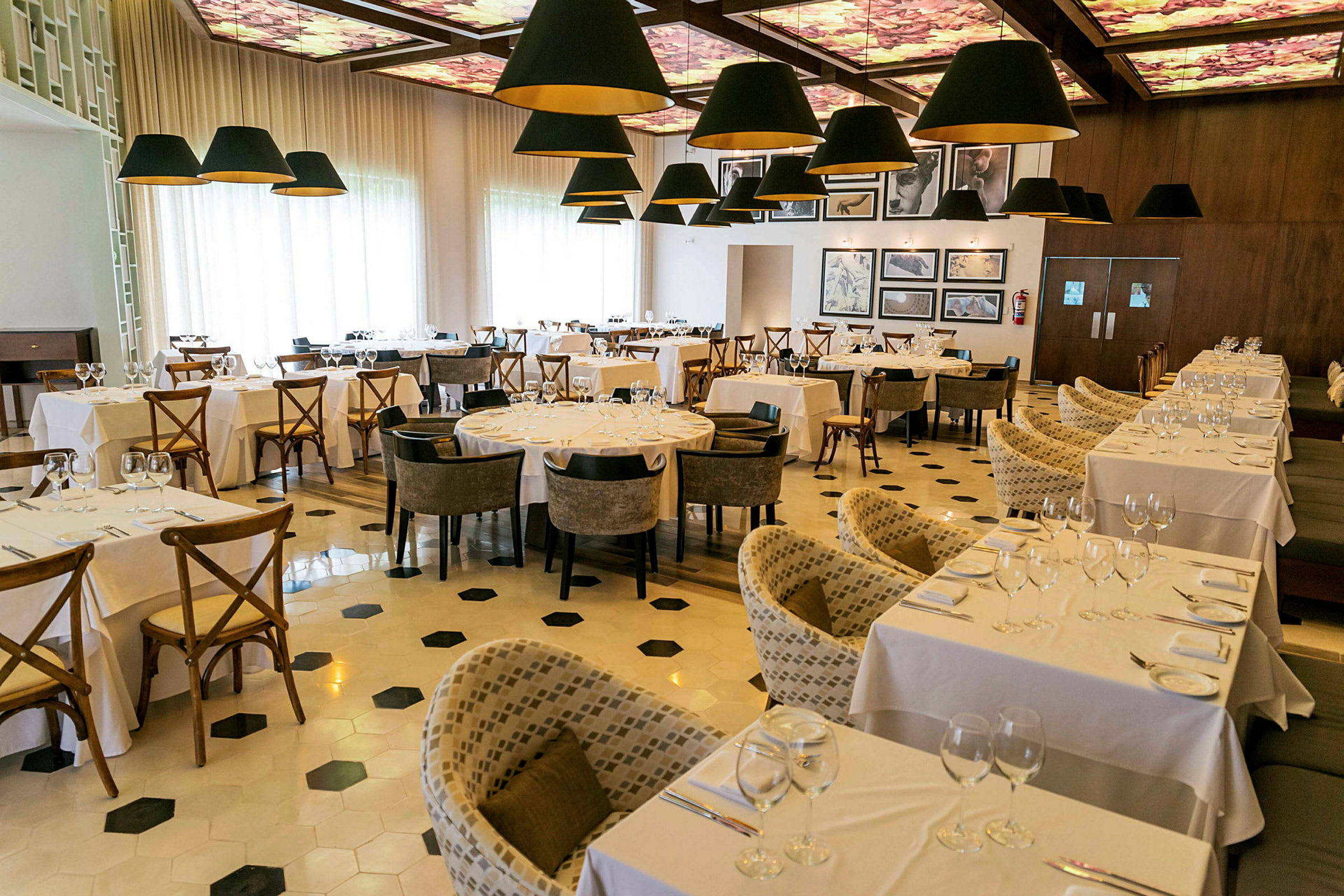 Bild av en elegant restaurang inredd med vita dukar på borden och bekväma stolar, med dekorativa lampor som hänger från taket. (AI-genererad text)