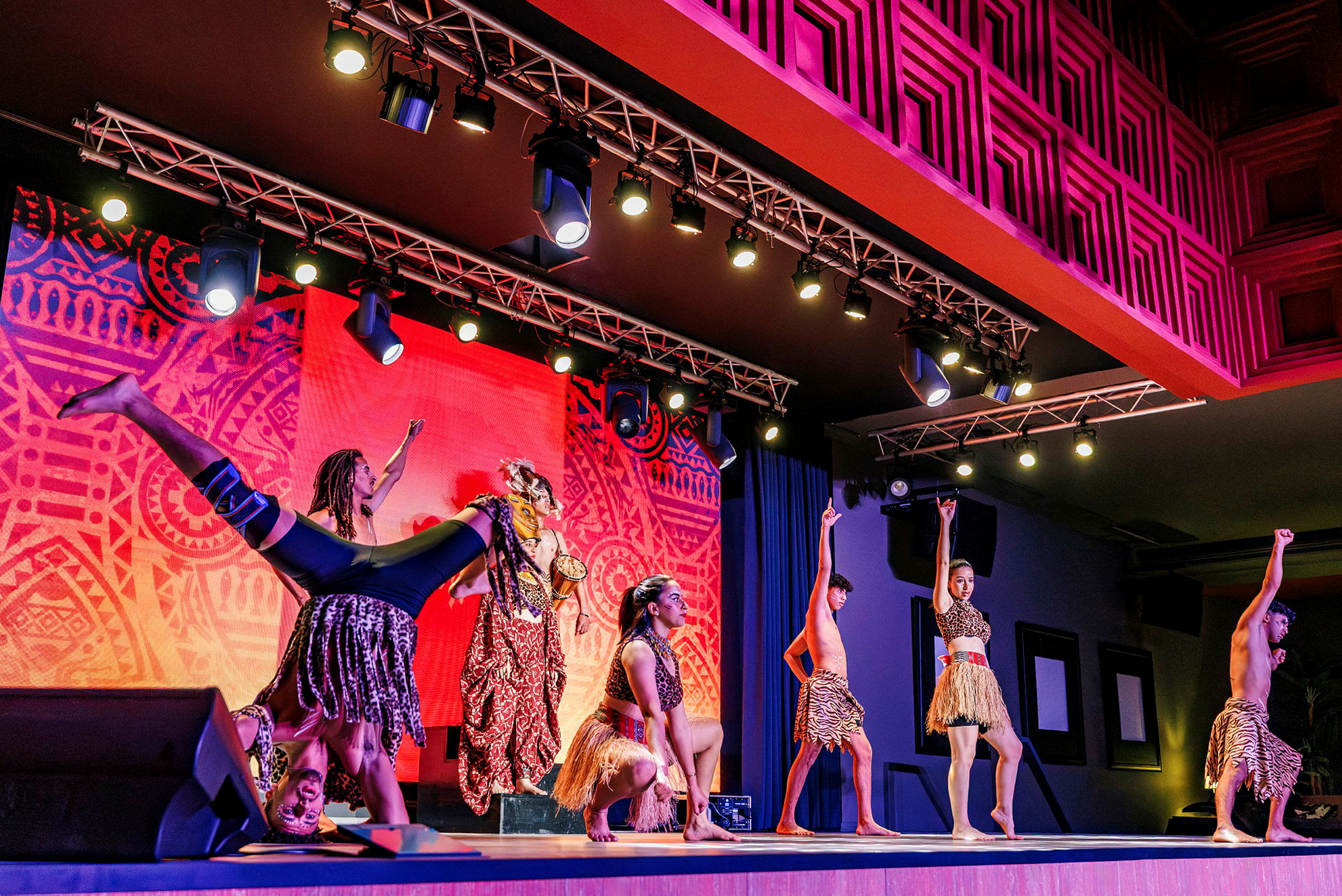 Grupp av dansare på scenen med ljus färgglad bakgrund och tribal-inspirerade kostymer. (AI-genererad text)