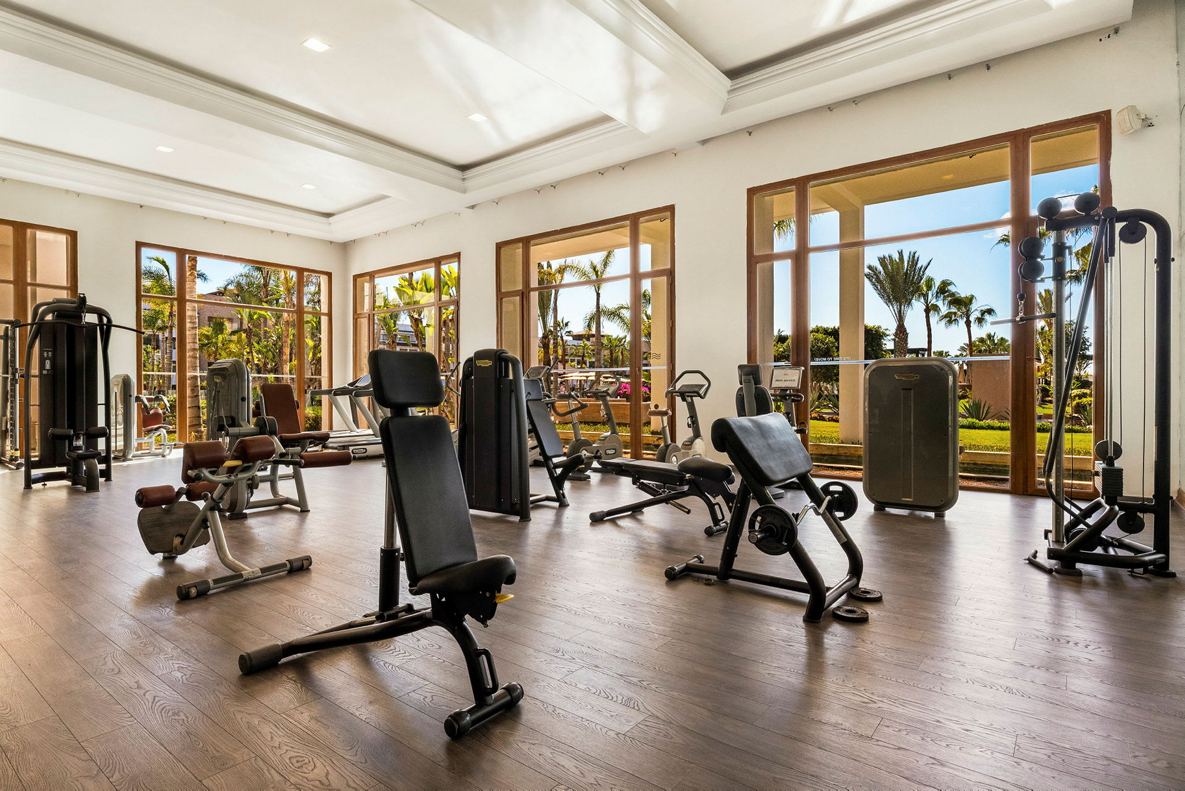 Ett gym med träningsutrustning mot fönster med utsikt över en trädgård. (AI-genererad text)