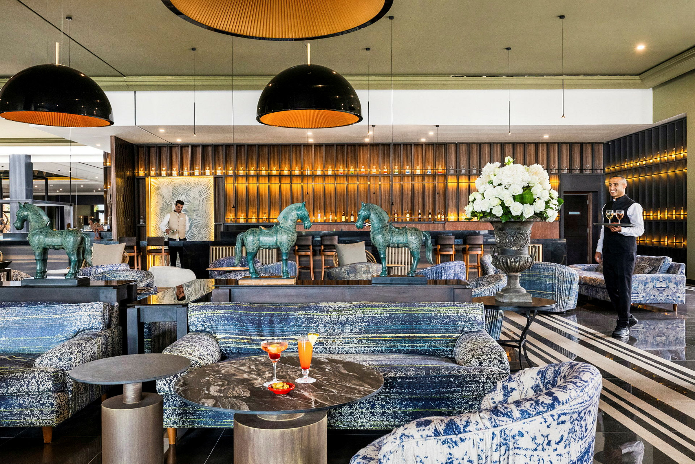 En stilfull lounge med soffor, marmorbord och dekorativa häststatyer, samt en bar belyst med varma ljus. (AI-genererad text)