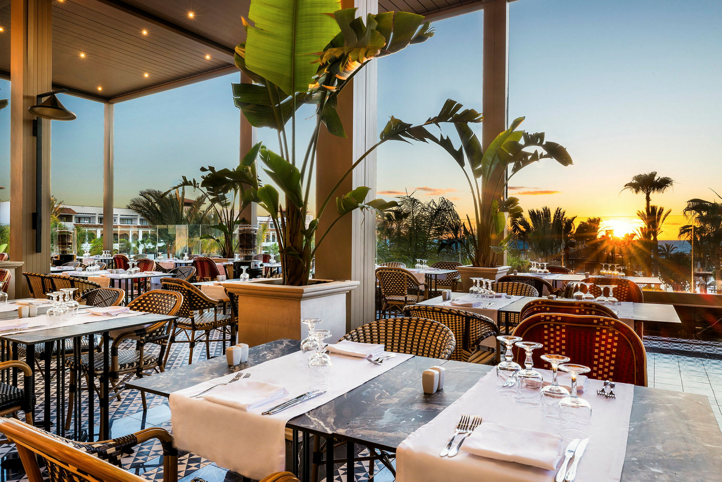 Restaurang med dukade bord och utsikt över solnedgången. (AI-genererad text)